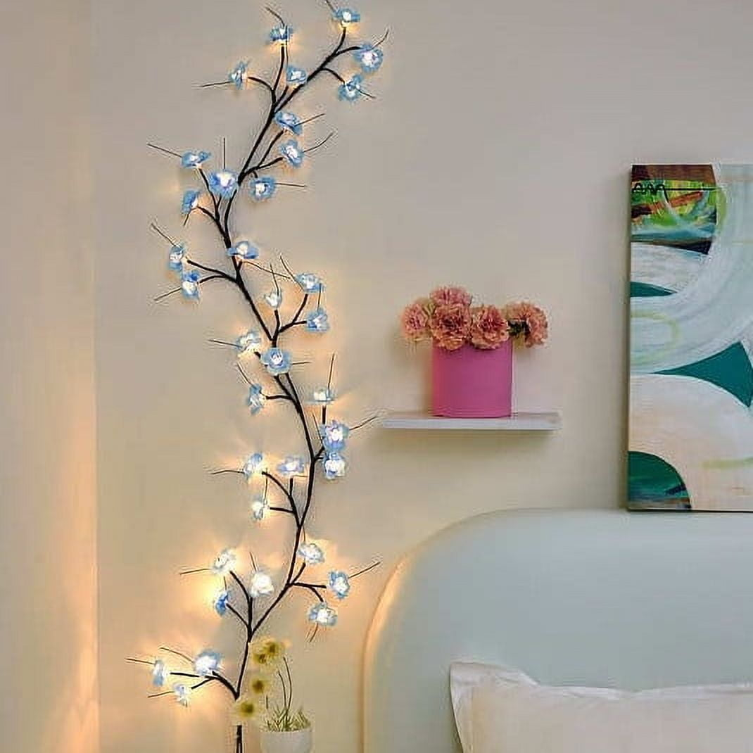 Eine Wand mit einem dekorativen Blumenast mit Lichtern, einem Regal mit rosa Blumen und einem Gemälde.