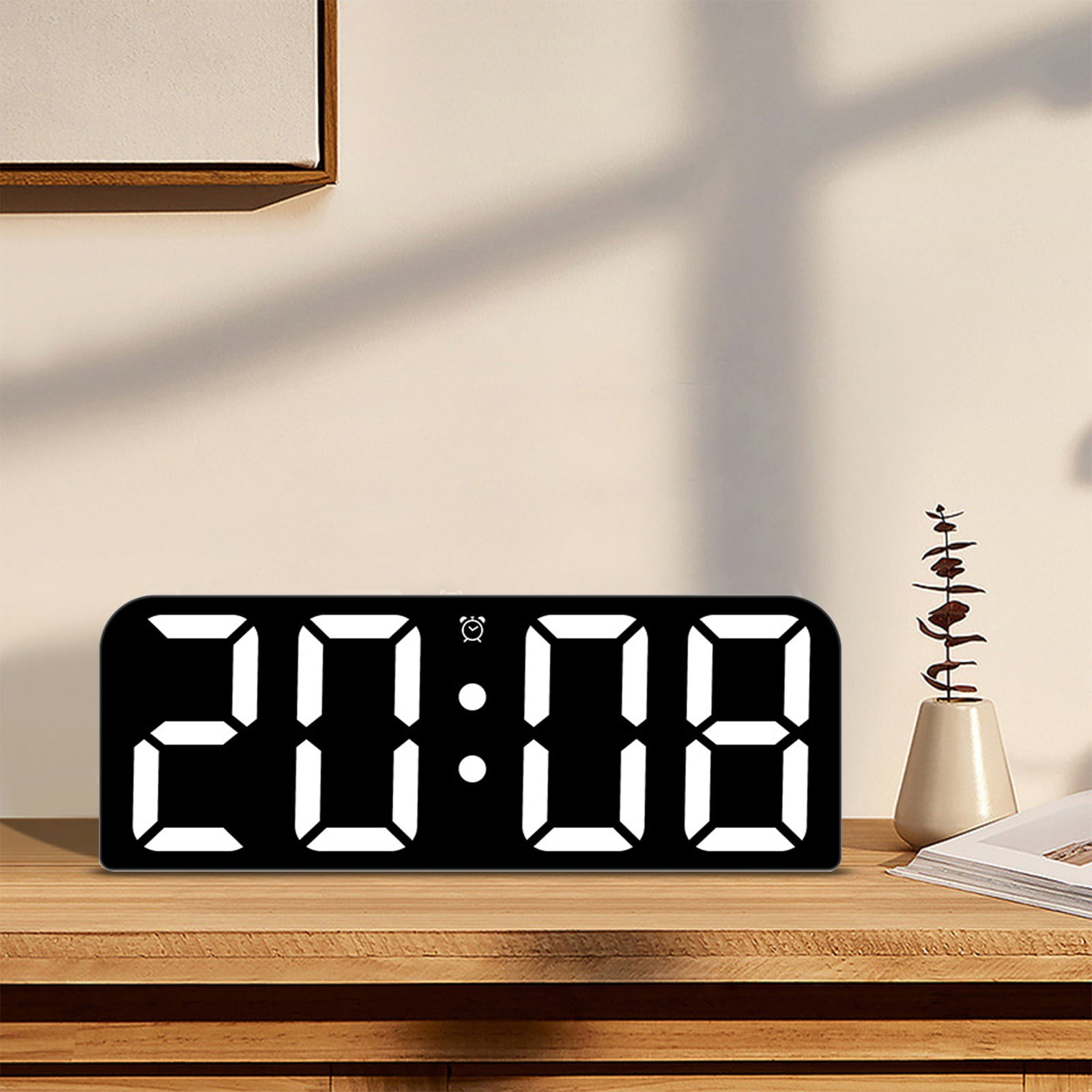 Eine Digitaluhr zeigt 20:08 in Weiß auf Schwarz an. Sie steht auf einer Holzoberfläche mit Vase und Buch.