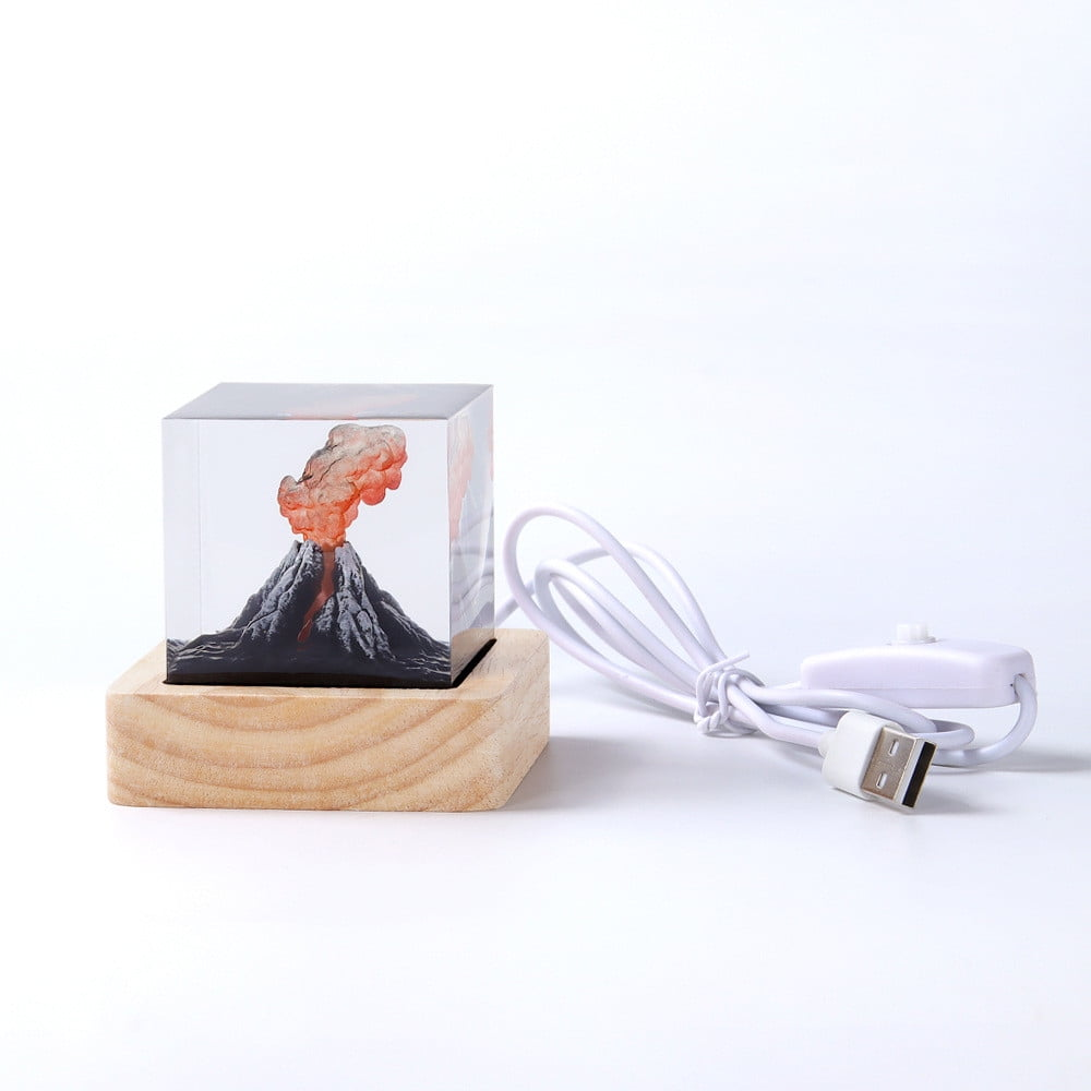 Eine dekorative Lampe mit einer Vulkanszene in einem durchsichtigen Würfel, auf einem Holzsockel. Ein weißes Kabel mit USB-Stecker und Schalter ist befestigt.