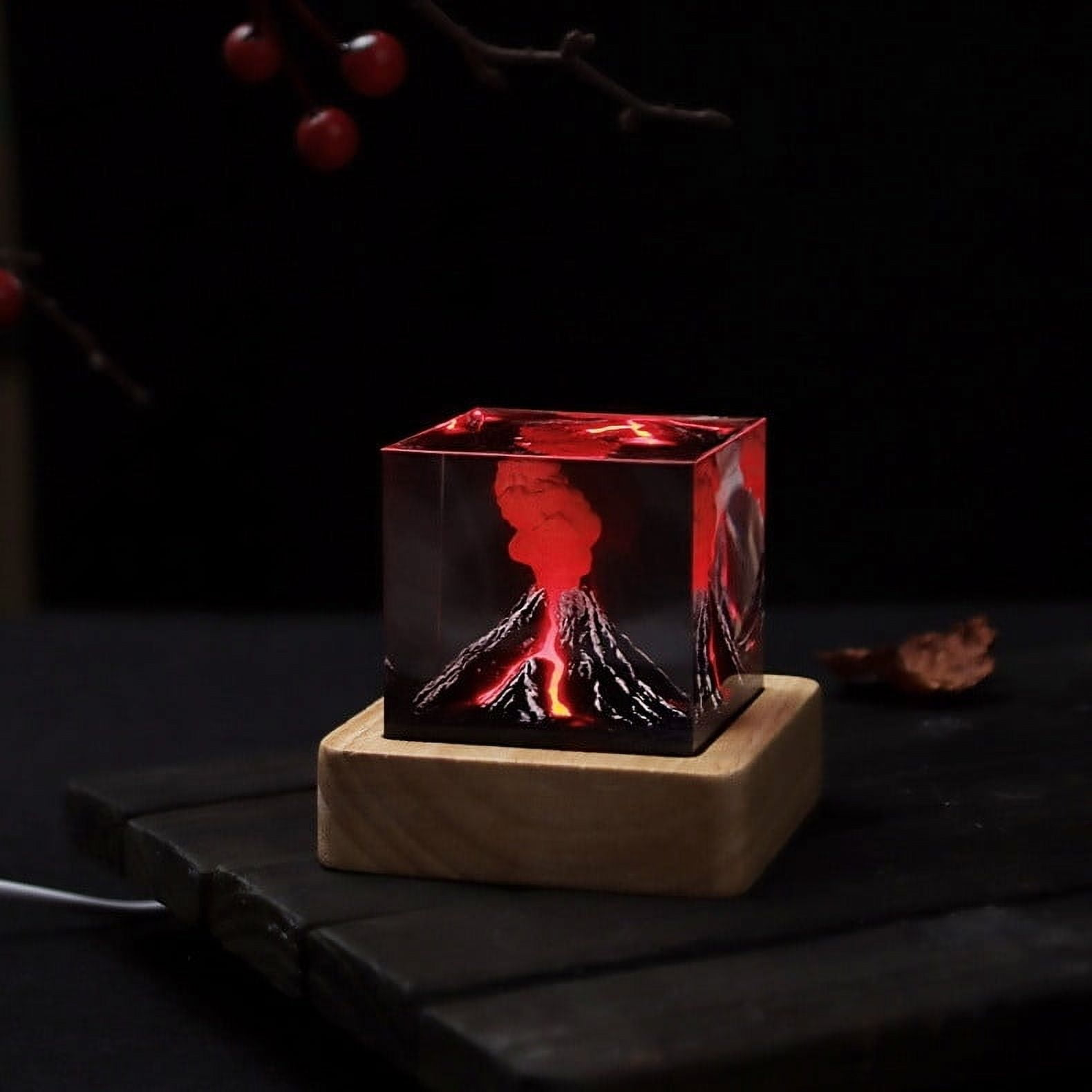 Eine leuchtende Vulkan-Skulptur in einem Glaskubus auf einem Holzsockel. Rote Lava bricht aus, vor dunklem Hintergrund.