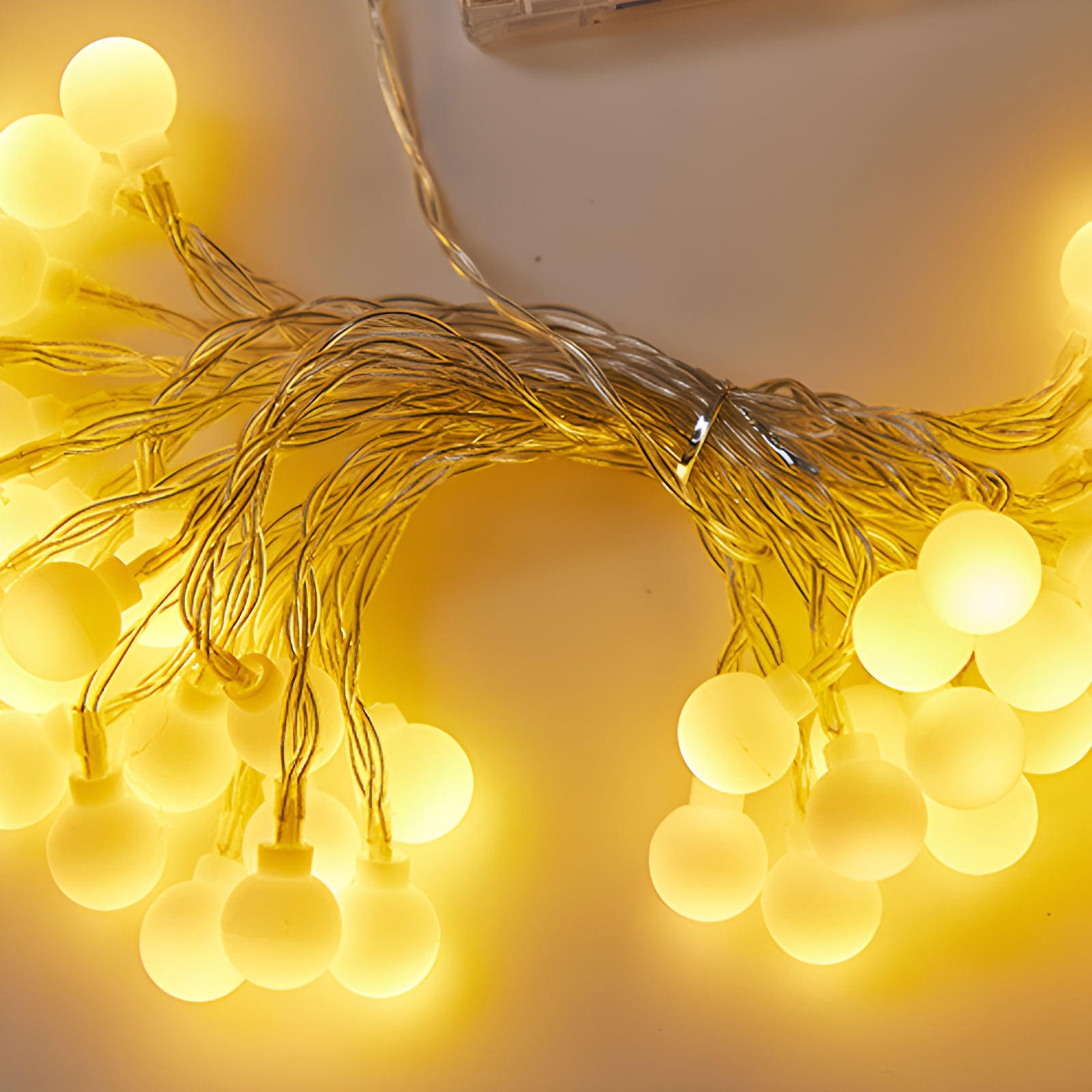 Lichterkette mit gelben Glühbirnen. Die Lichter sind eingeschaltet und in einem Bündel angeordnet. Der Hintergrund ist hellbeige.