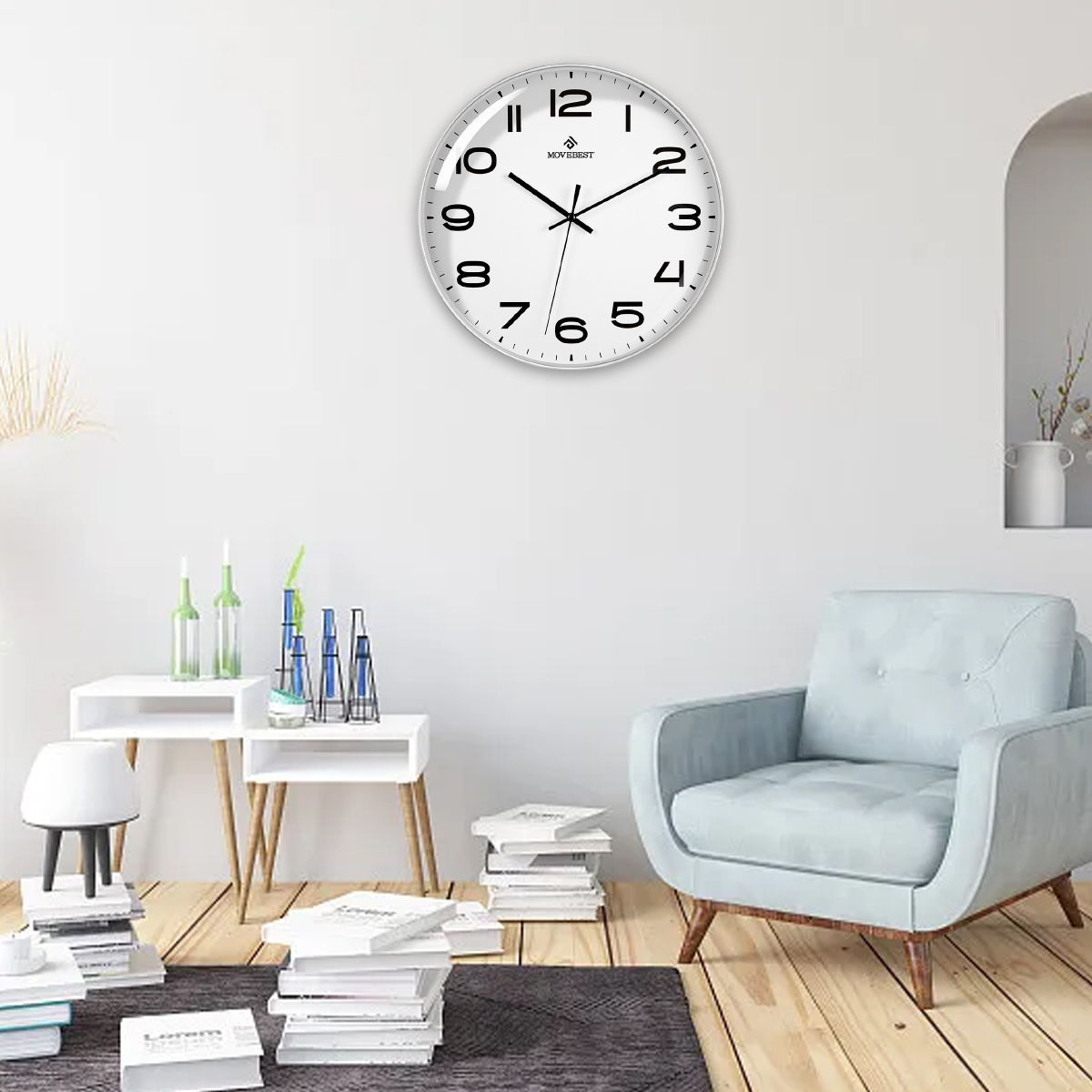 Eine weiße Wanduhr hängt an einer weißen Wand. Ein hellblauer Sessel, Bücher und Dekorationen befinden sich im Raum.