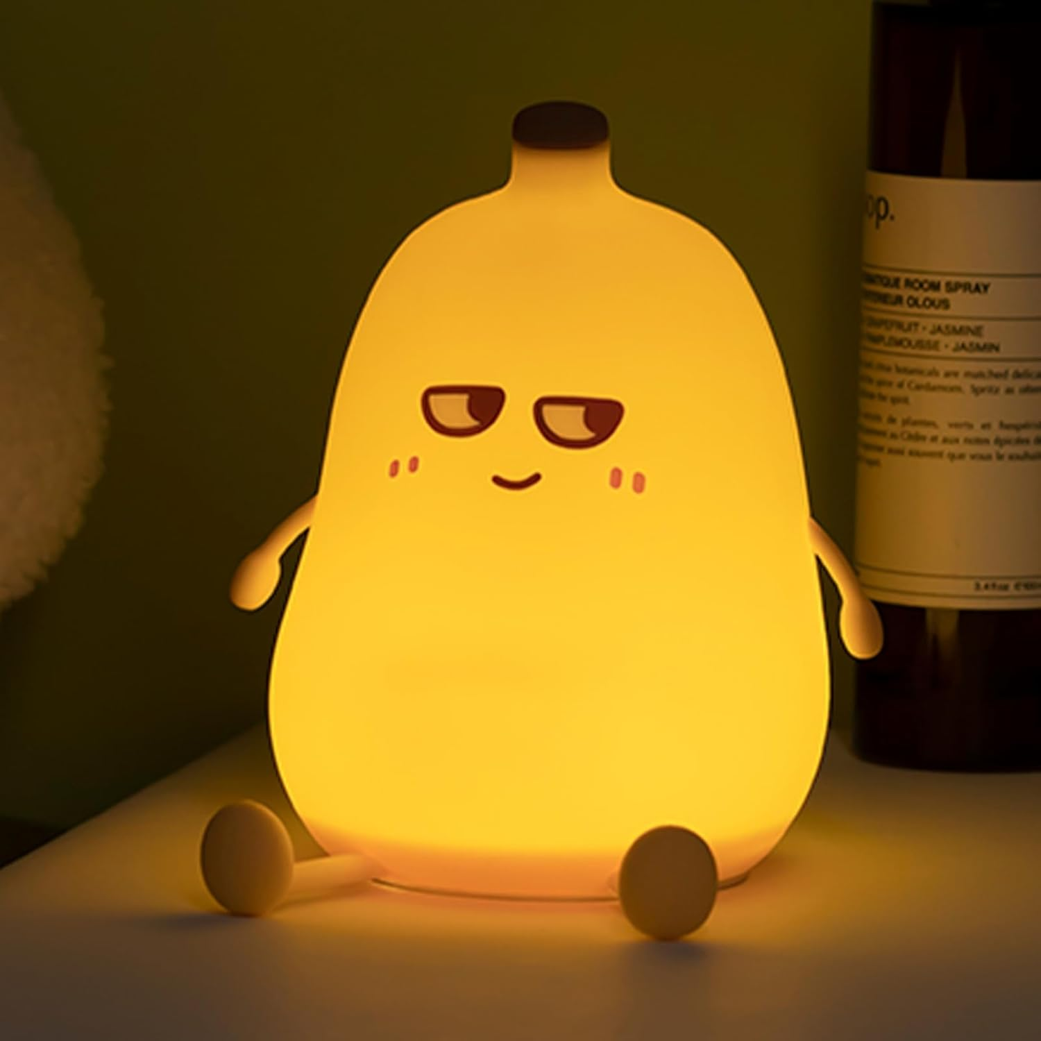 Ein gelbes, cartoonartiges Nachtlicht mit Armen, Beinen und einem Gesicht. Hinter der Lampe steht eine braune Flasche.