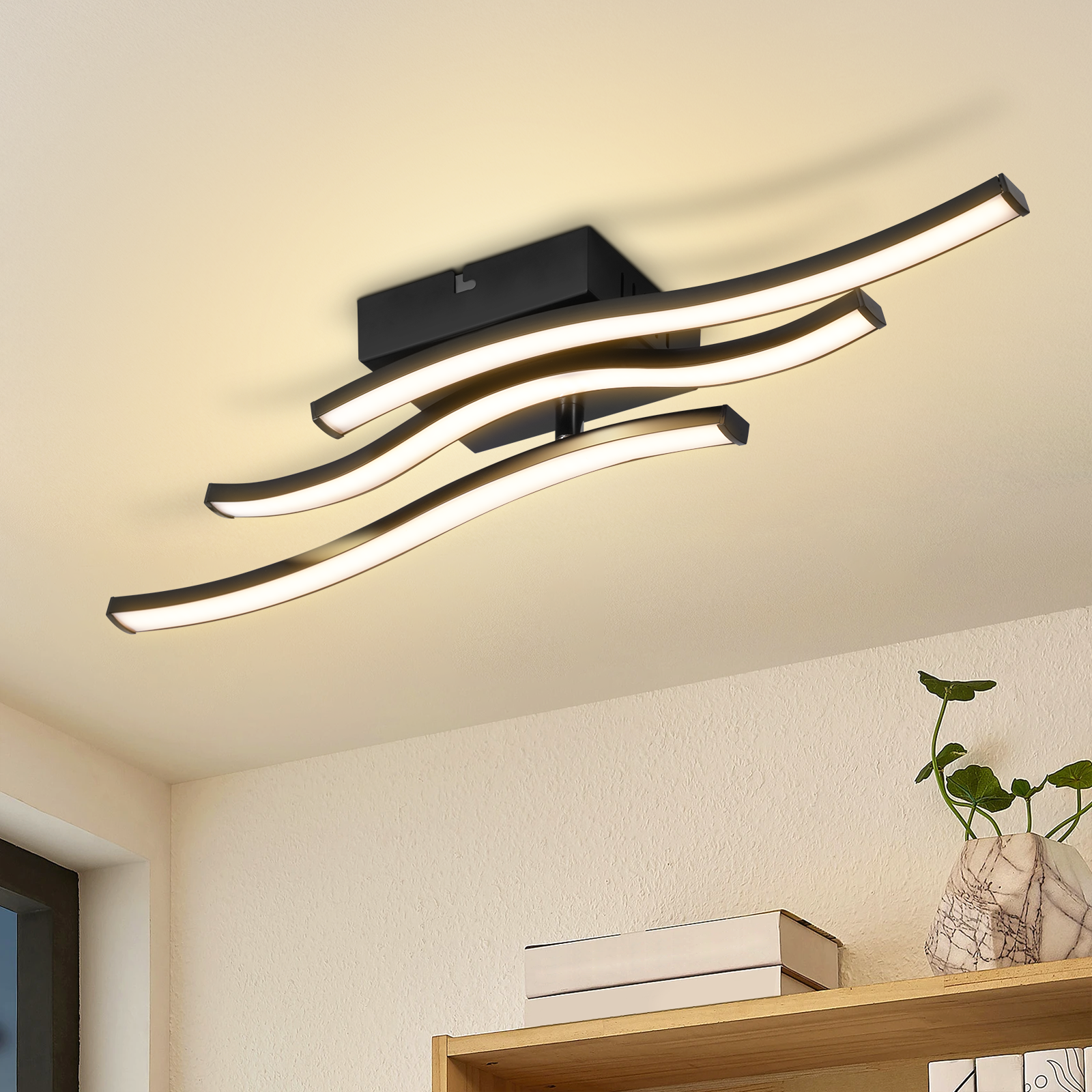 Nowoczesna lampa sufitowa z zakrzywionymi czarnymi elementami i jasnymi białymi światłami. Książki i roślina znajdują się na półce poniżej.