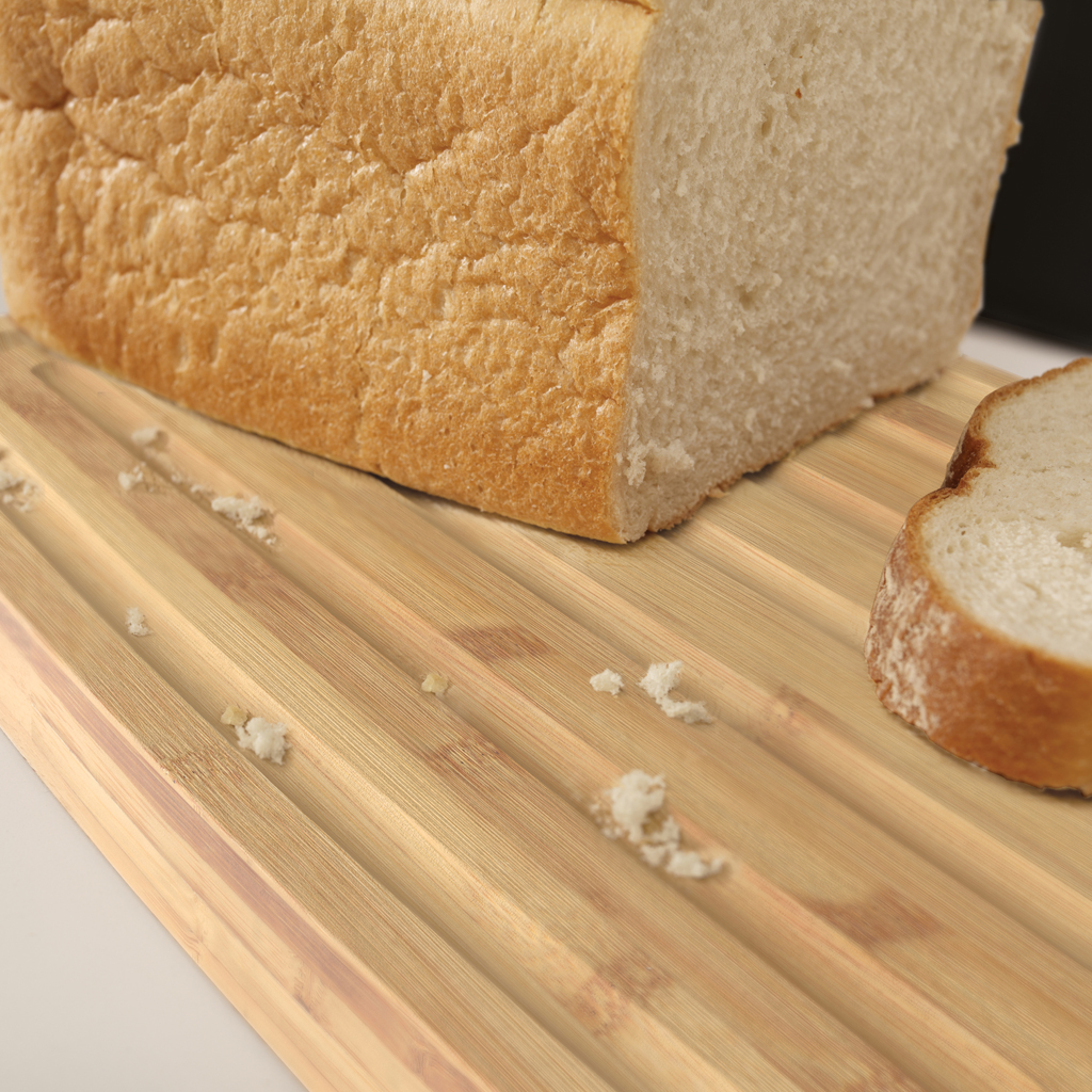 Ein Brotlaib mit einer Scheibe auf einem Holzschneidebrett, Krümel verstreut. Das Brot ist hellbraun.