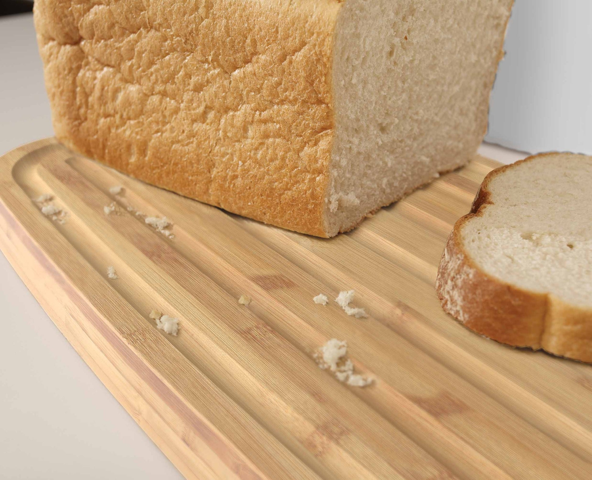 Ein Brotlaib mit einer Scheibe auf einem Holzbrett. Brotkrümel sind auf dem Brett verstreut.