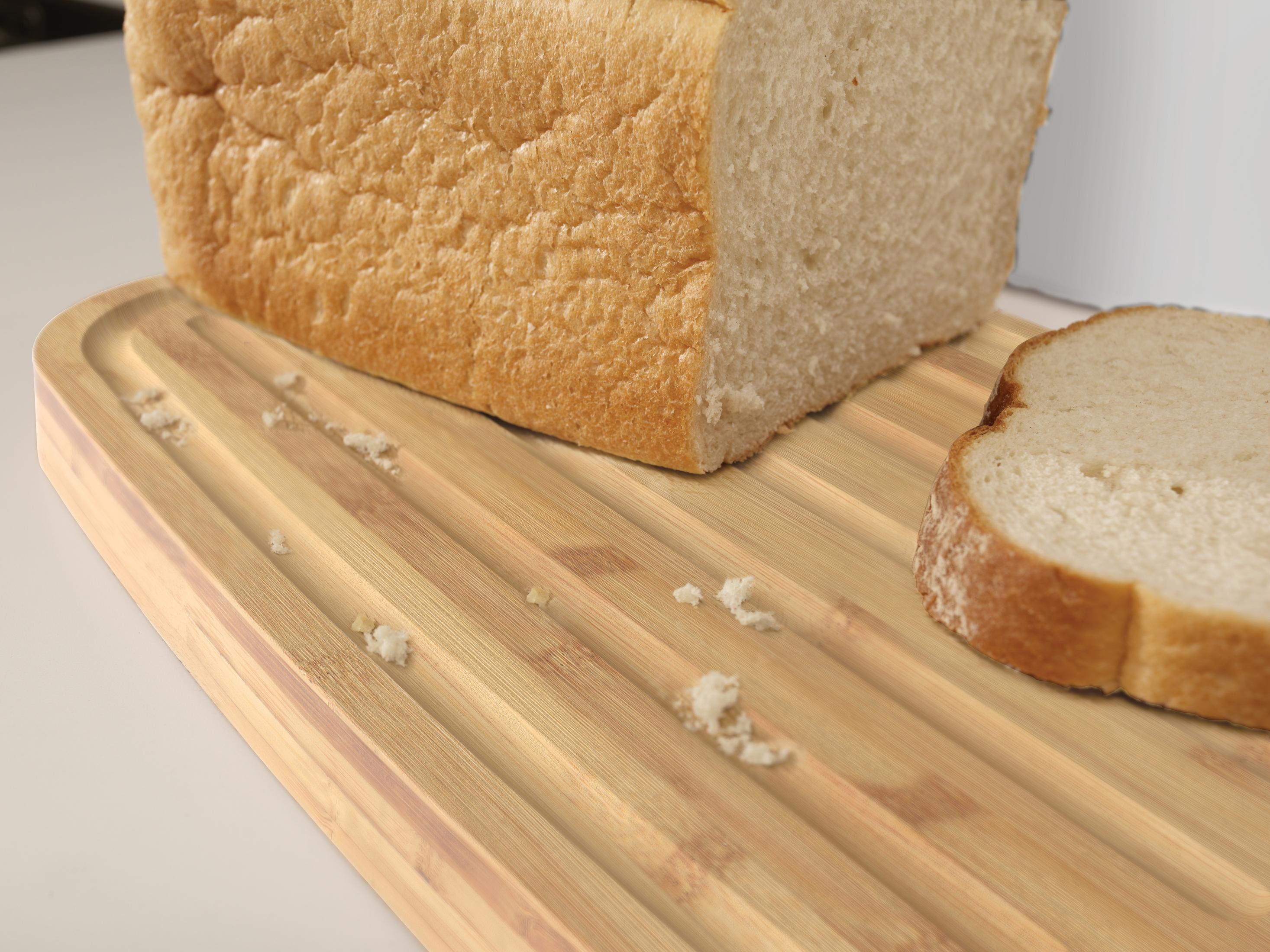 Ein Brotlaib mit einer abgeschnittenen Scheibe liegt auf einem Holzschneidebrett. Brotkrumen sind verstreut.