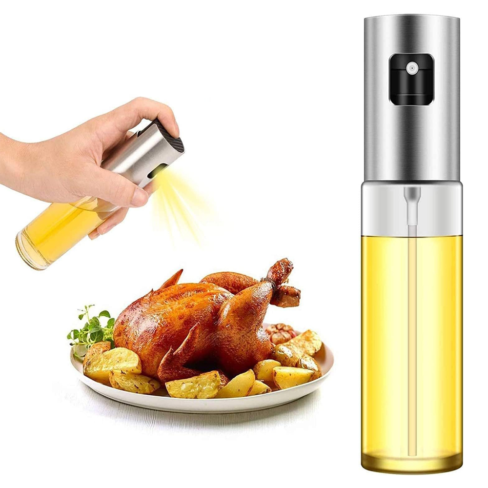Eine Hand sprüht Öl auf ein gebratenes Huhn und Kartoffeln. Rechts befindet sich ein Ölsprüher. Das Essen ist auf einem weißen Teller.
