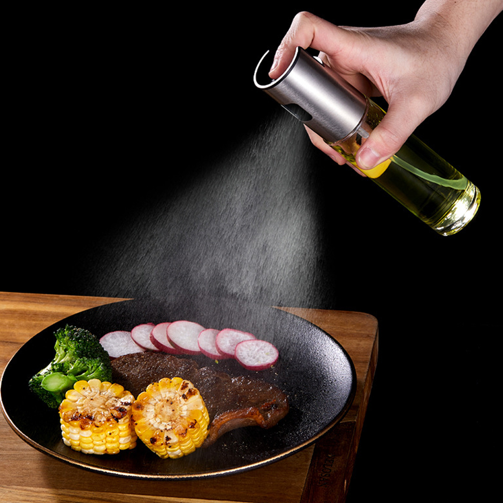 Eine Hand sprüht Öl auf einen Teller mit Steak, Mais, Radieschen und Brokkoli. Schwarzer Hintergrund, Holzoberfläche.