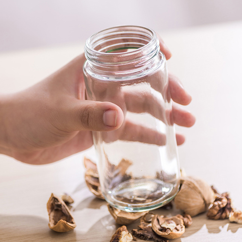 Eine Hand hält ein klares Glas. Walnüsse und Schalen liegen auf einer Holzoberfläche verstreut.