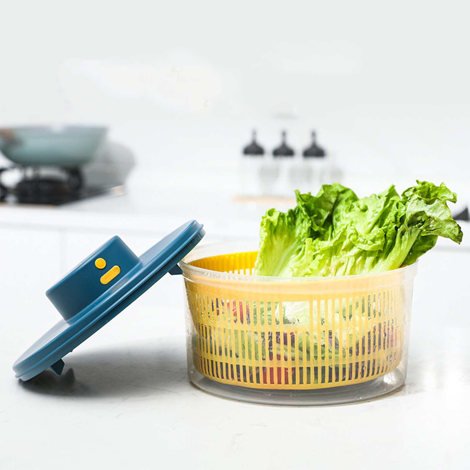 Ein Salat-Spinner mit Salat. Der Deckel ist offen. Küchenhintergrund mit einigen Objekten.