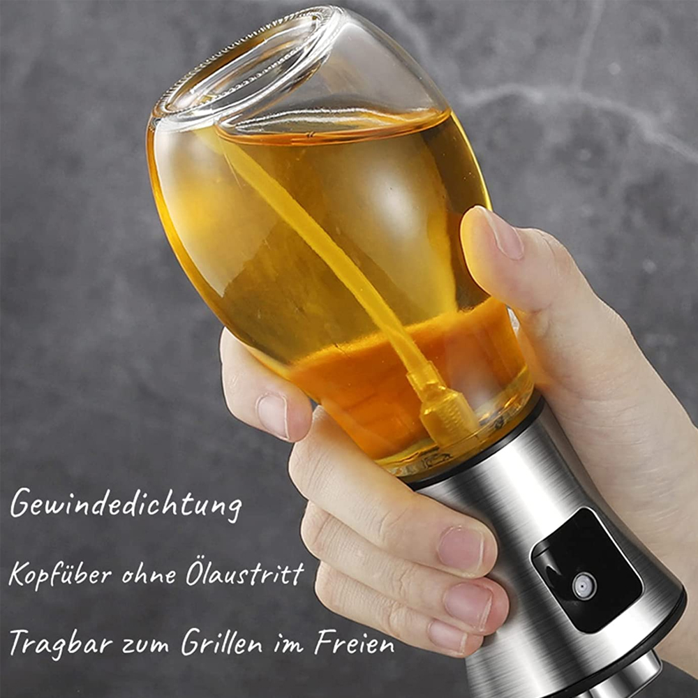 Eine Hand hält einen Glasölsprüher, der mit gelber Flüssigkeit gefüllt ist. Der Sprüher hat einen Edelstahlfuß. Der Hintergrund ist grau.