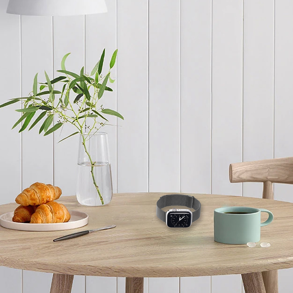 Ein Tisch mit Croissants, einer Uhr, einer Tasse und einer Vase mit Grünzeug. Der Hintergrund ist eine weiße Wand.