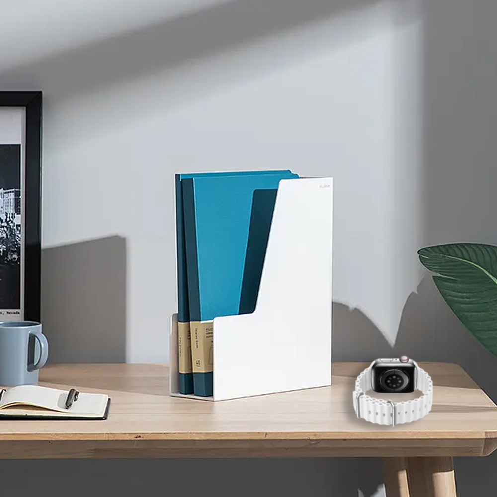 Weißer Zeitschriftenhalter mit teal Ordnern. Eine Uhr und ein Notizbuch liegen auf dem Holztisch, mit einem gerahmten Bild und einer Tasse.