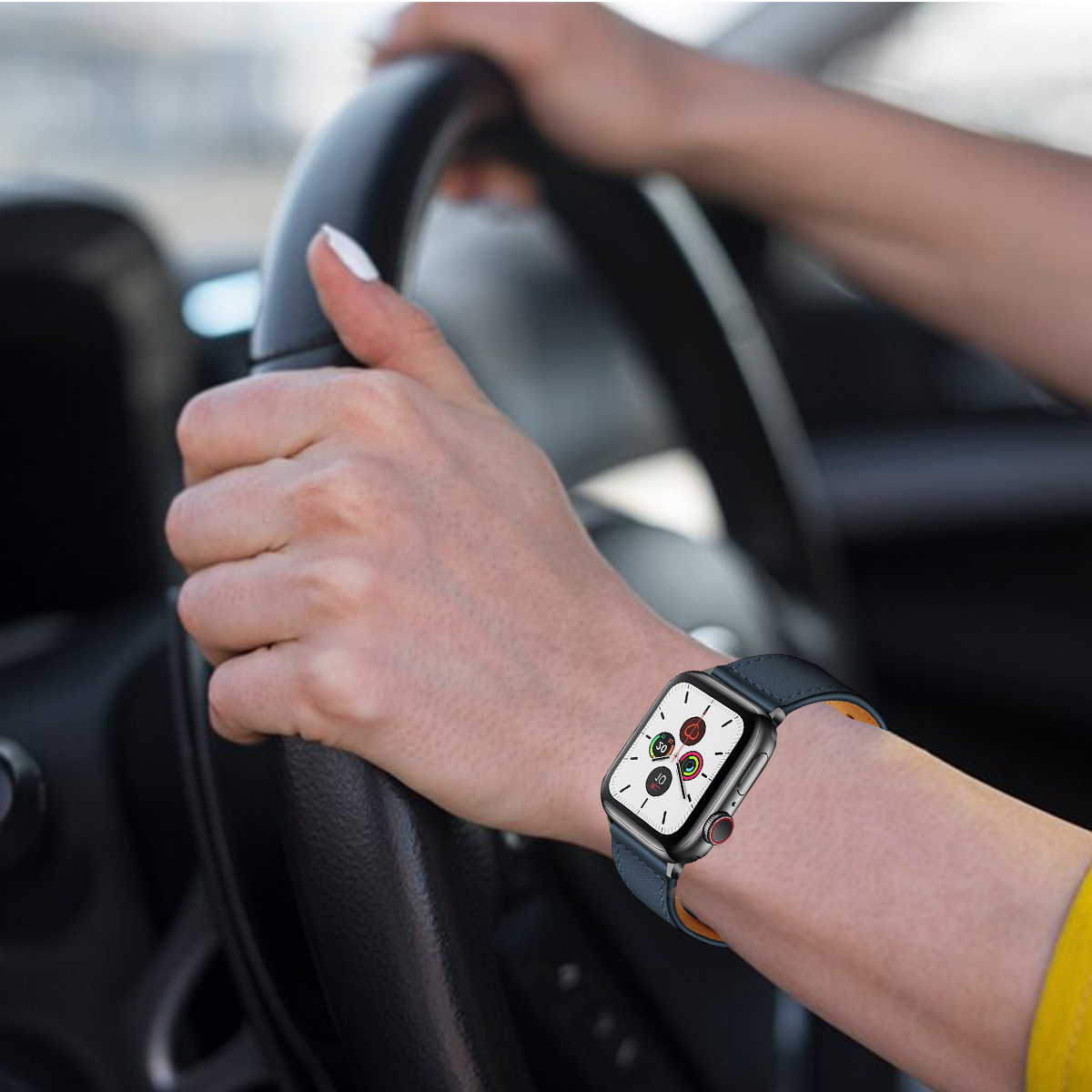 Person fährt Auto, Hände am Lenkrad. Eine Smartwatch ist am Handgelenk mit blauem Lederarmband sichtbar.