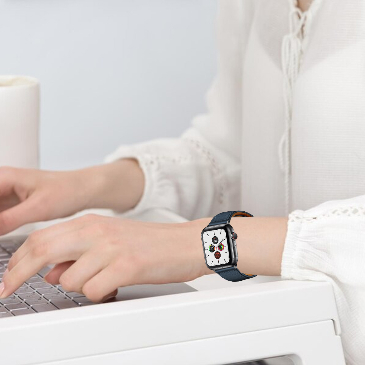 Eine Person trägt eine blaue Smartwatch mit weißem Zifferblatt. Sie tippt auf einem Laptop. Weißes Hemd und Hintergrund.