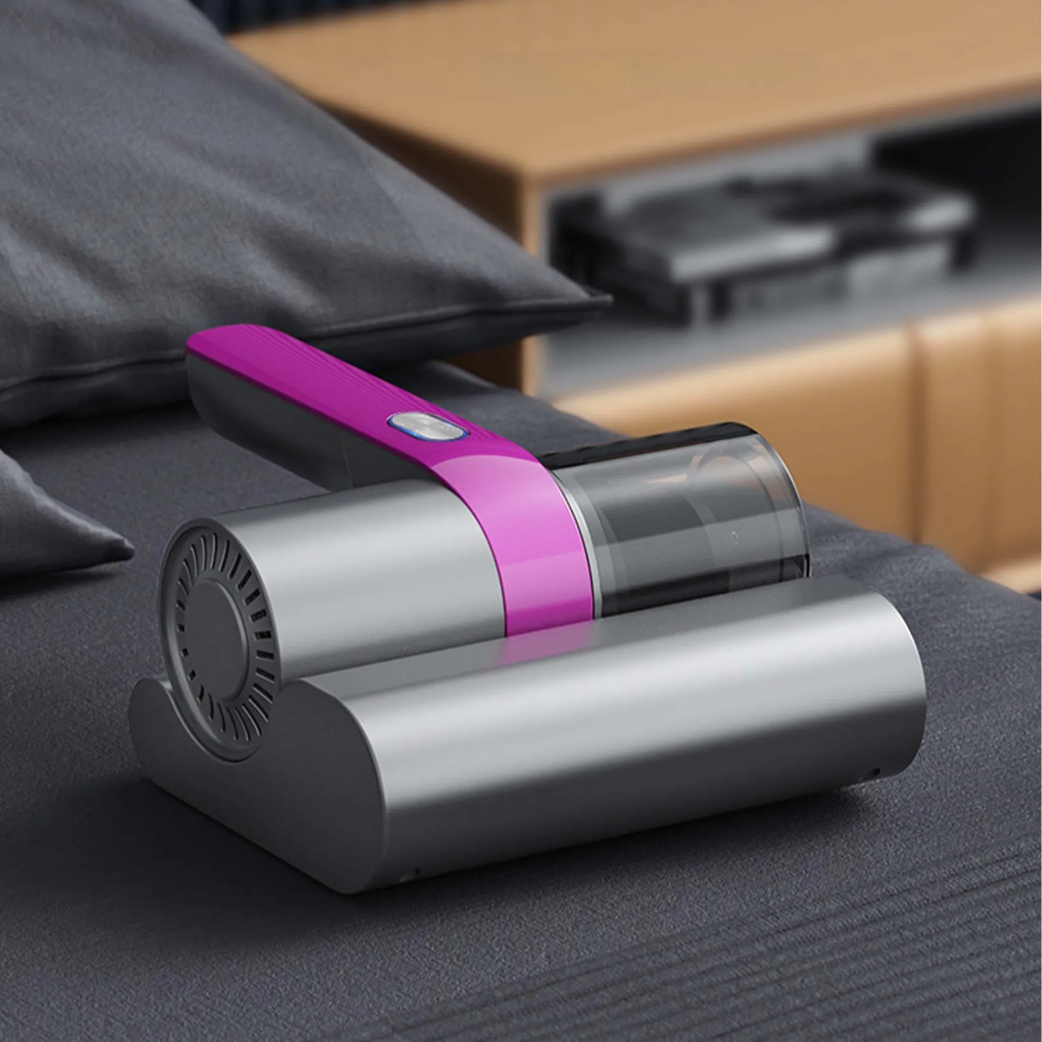 Ein Handstaubsauger mit pinkfarbenem Griff liegt auf einem Bett. Er ist silber und schwarz. Im Hintergrund befindet sich ein Nachttisch.