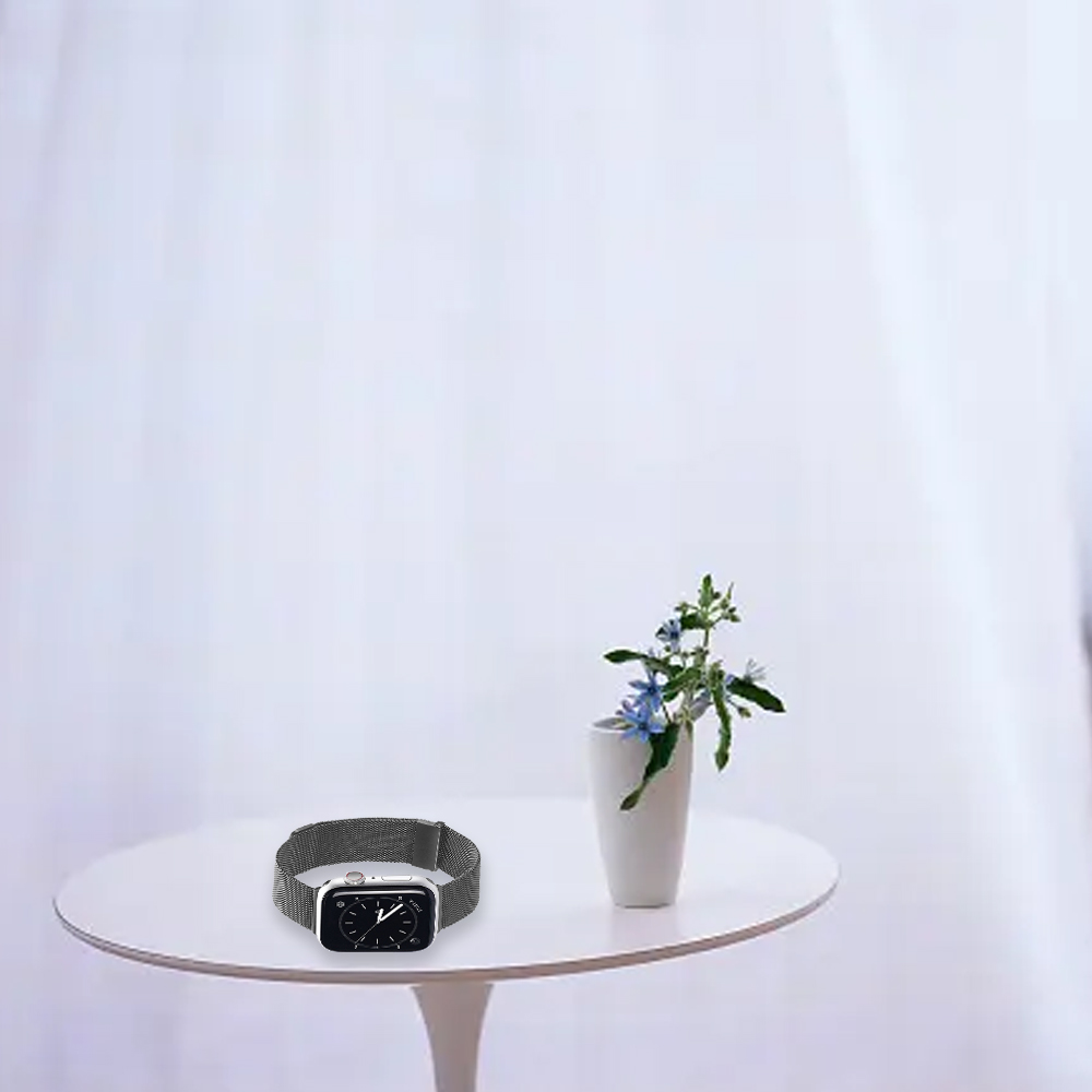 Eine Apple Watch mit silbernem Armband liegt auf einem weißen Tisch. Eine weiße Vase hält Blumen. Weißer Vorhang im Hintergrund.