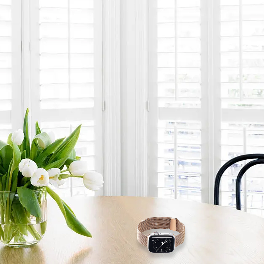 Ein Tisch mit einer Vase mit weißen Tulpen, einer Apple Watch und einem Fenster mit weißen Fensterläden.