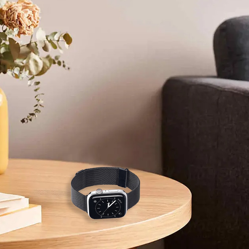 Eine Apple Watch mit schwarzem Armband liegt auf einem Holztisch. Eine Vase mit Blumen und eine Couch sind ebenfalls im Bild.