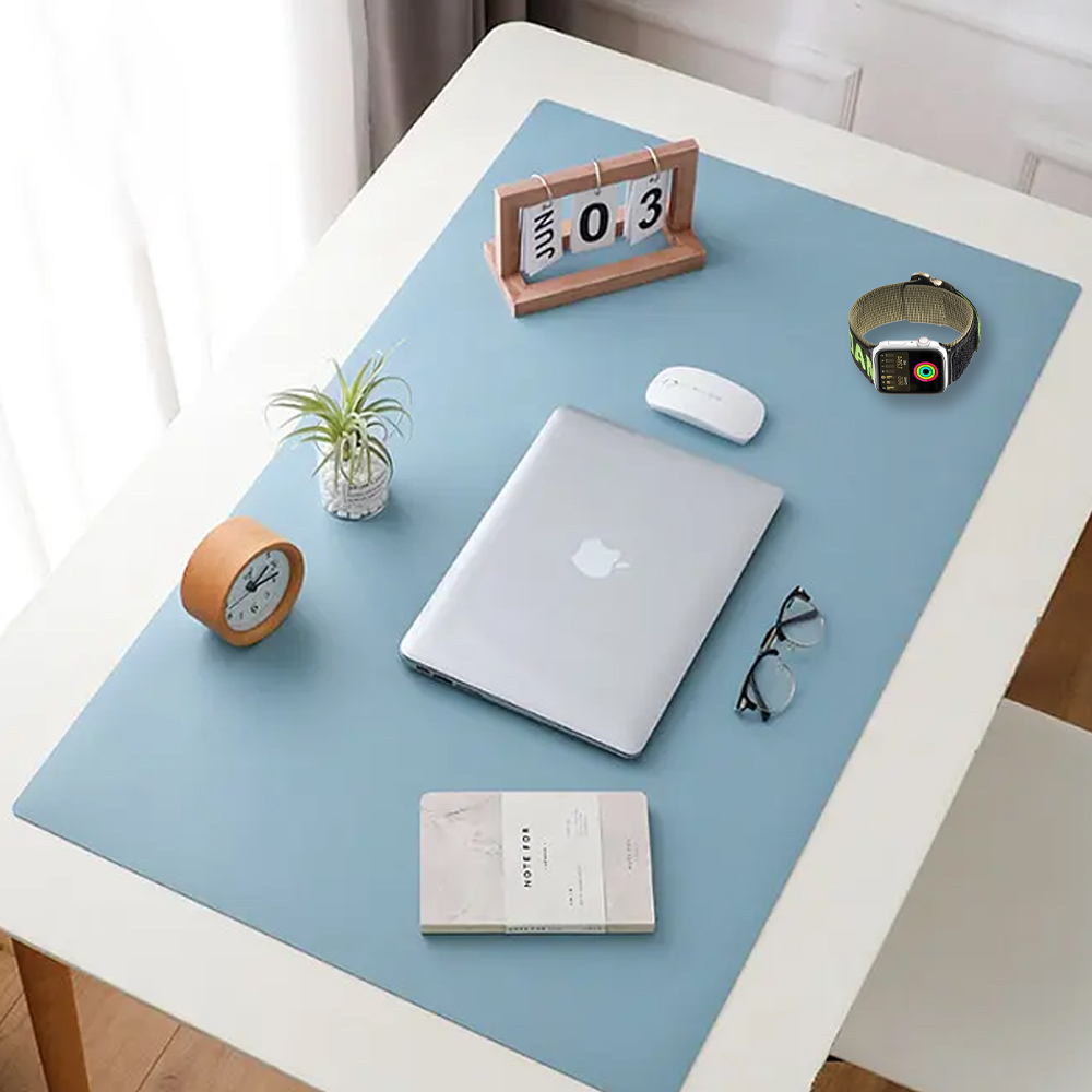 Ein Schreibtisch mit blauer Matte. Artikel sind Laptop, Uhr, Brille, Uhr, Kalender, Maus, Notizblock und Pflanze.