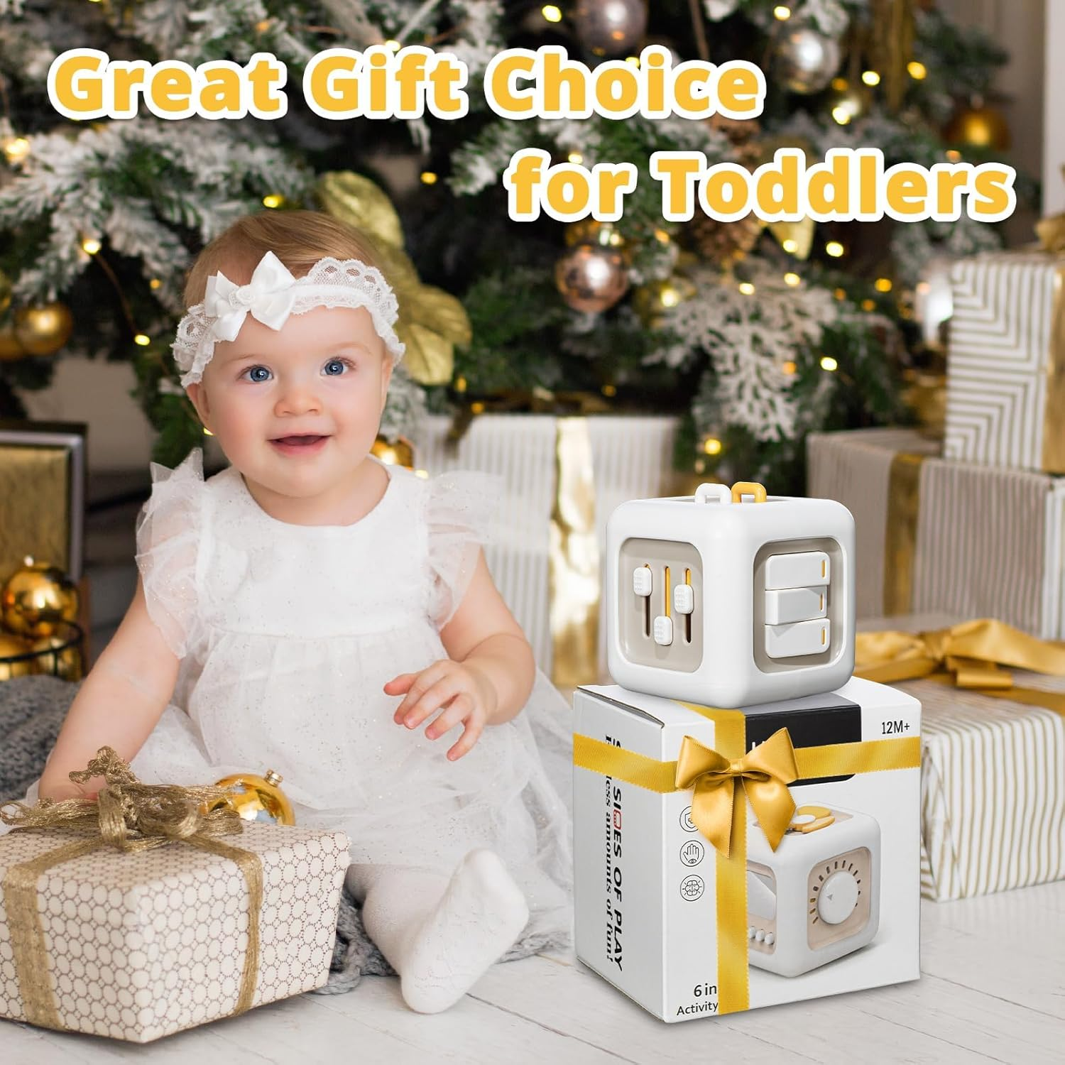 Ein Baby in einem weißen Kleid sitzt in der Nähe von Geschenken und einem Spielzeugwürfel. Der Text lautet 'Great Gift Choice for Toddlers'. Im Hintergrund ist ein Weihnachtsbaum zu sehen.