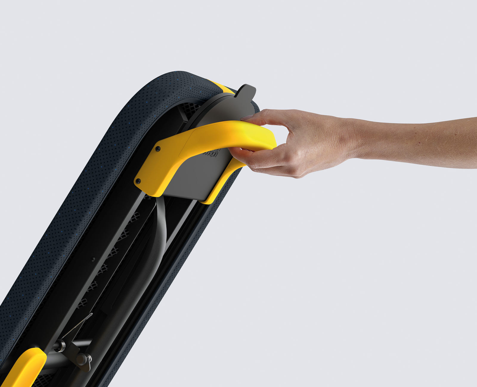 Una mano sostiene una manija amarilla en un objeto negro y amarillo con una superficie azul punteada. El fondo es gris.