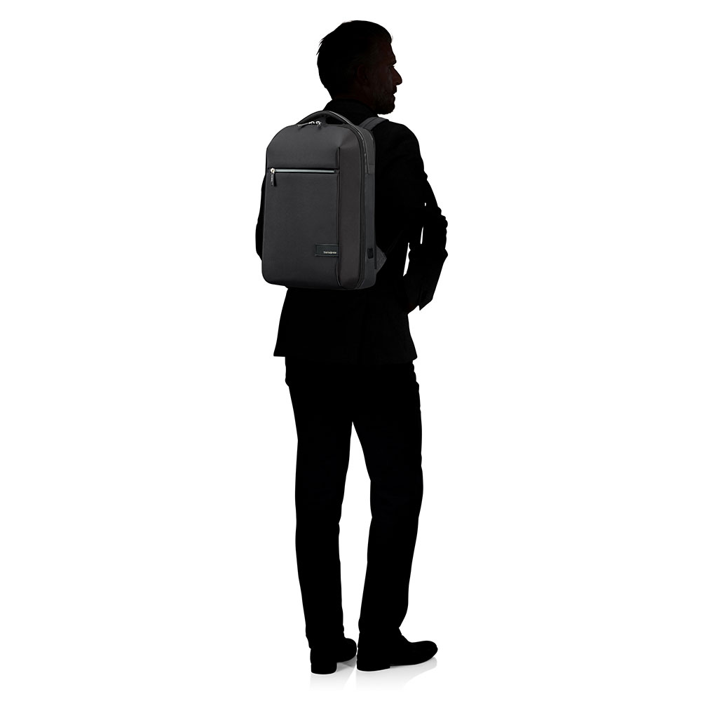 Un hombre con traje está de espaldas al espectador, con una mochila negra. El fondo es blanco.