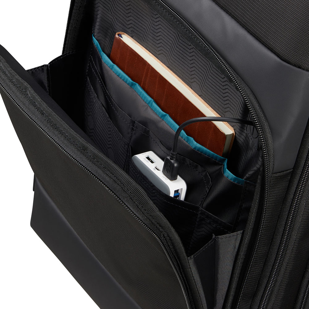 Schwarzes Rucksackinnere mit Taschen. Ein Notizbuch, ein weißes Ladegerät und ein Ladekabel befinden sich in den Taschen. Blaue Akzente sind sichtbar.