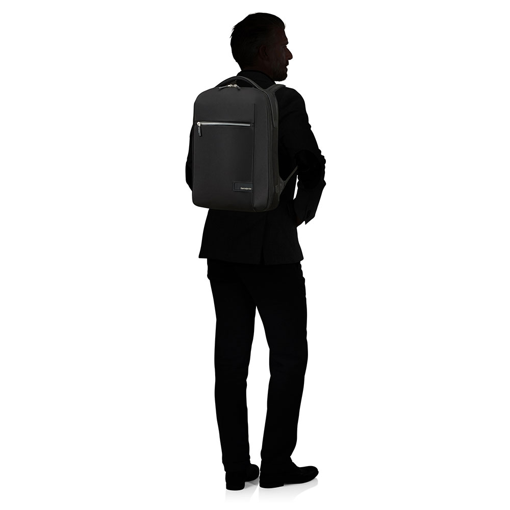 Ein Mann in einem schwarzen Anzug steht mit dem Rücken zugewandt und trägt einen schwarzen Rucksack. Der Hintergrund ist weiß.