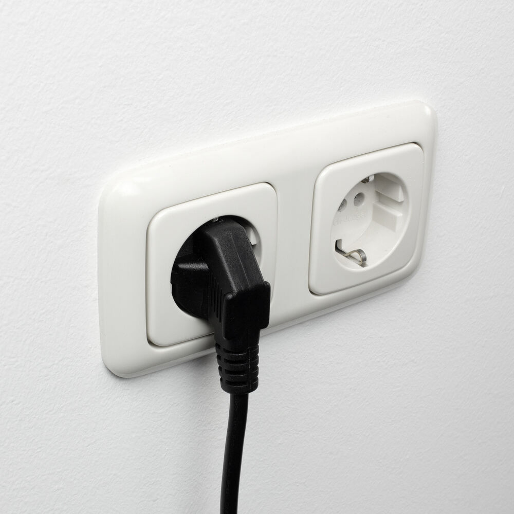 A white electrical outlet with a black plug inserted. The outlet is mounted on a white wall. One socket is in use.