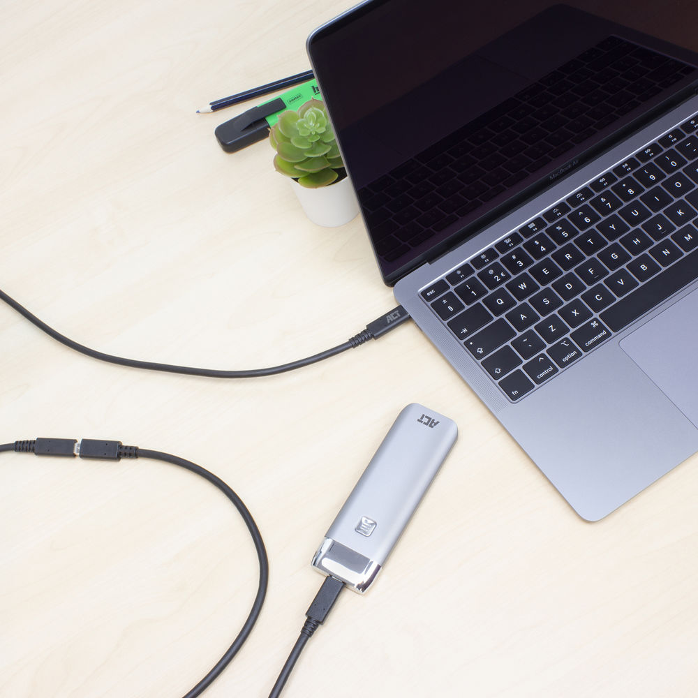 Een laptop verbonden met een zilveren externe harde schijf. Een kabel loopt van de schijf naar de laptop. Een kleine plant en kantoorbenodigdheden zijn zichtbaar.