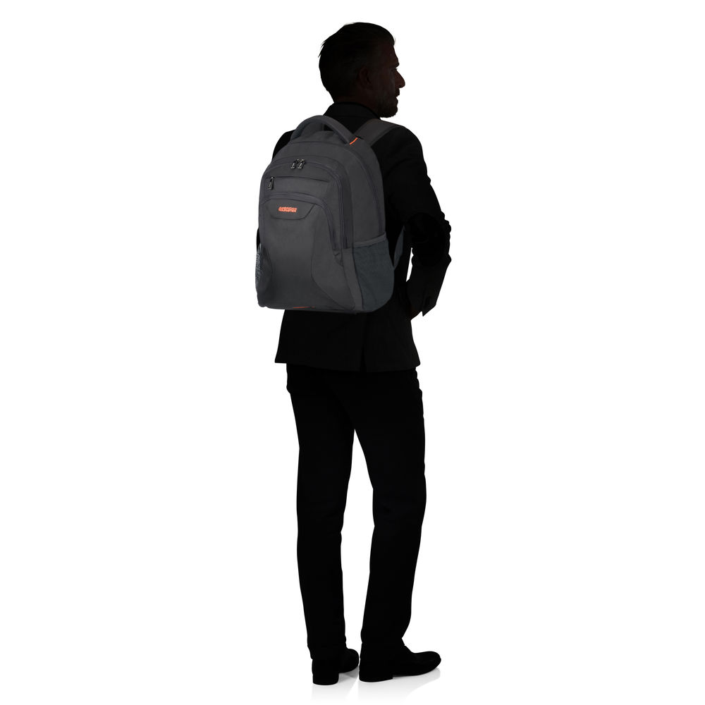 Ein Mann im schwarzen Anzug steht abgewandt. Er trägt einen Rucksack. Der Hintergrund ist weiß.