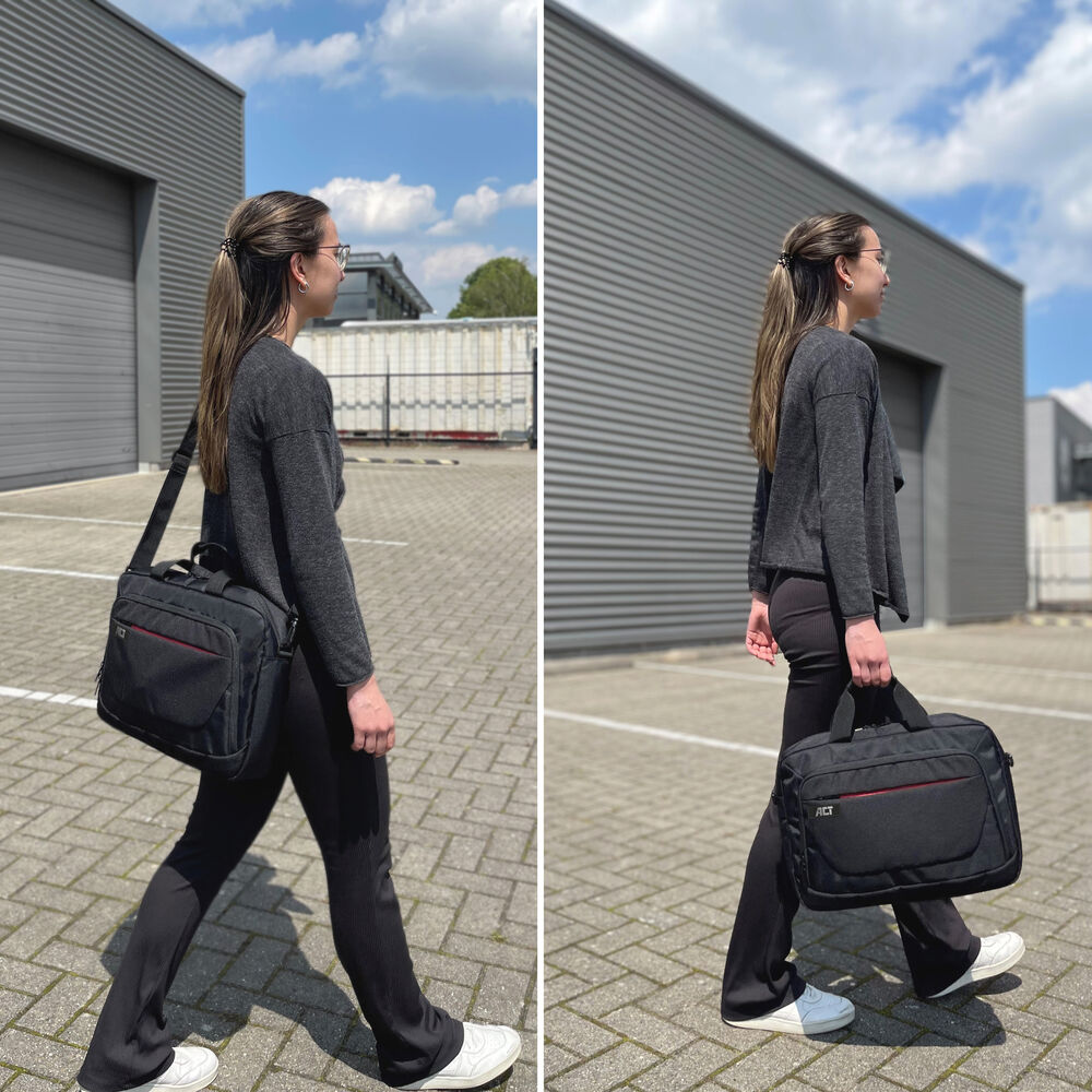 Una donna cammina con una borsa nera. Indossa pantaloni neri, una giacca grigia e scarpe bianche. Edifici e cielo blu sullo sfondo.