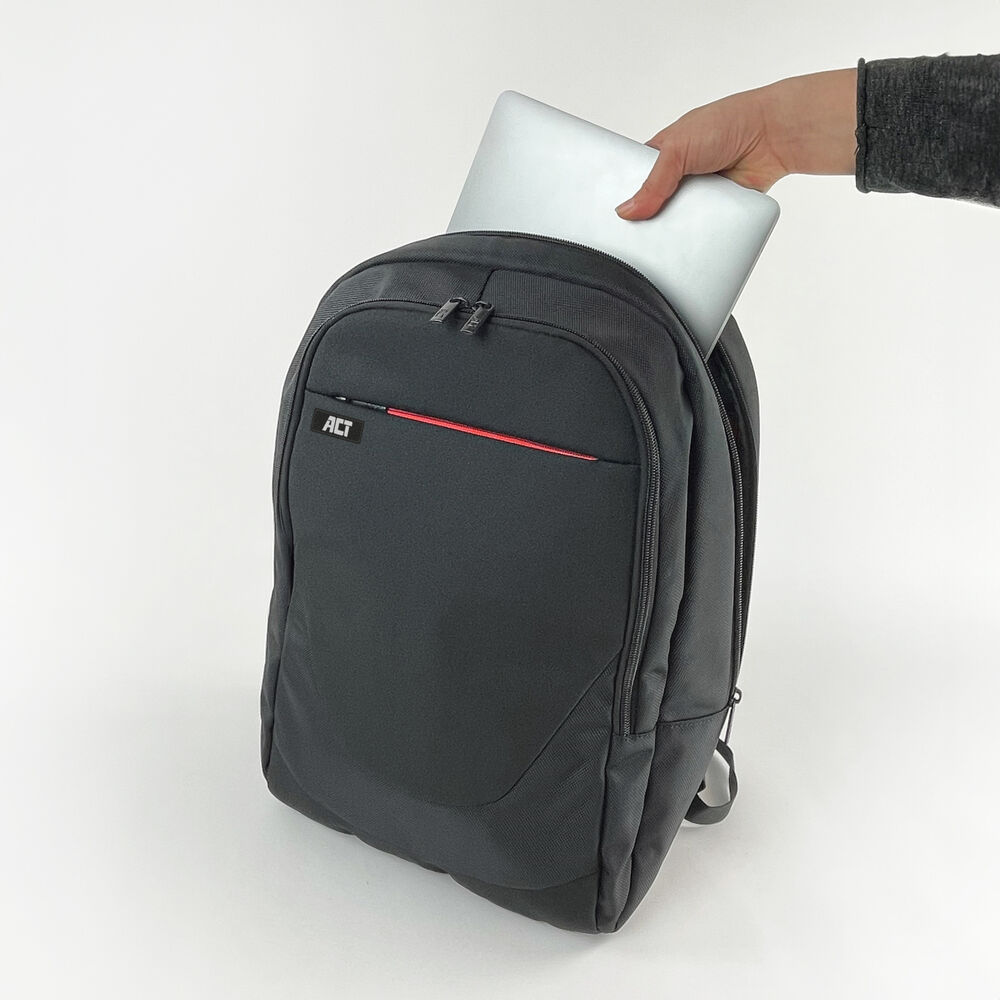 Una persona sta mettendo un laptop argentato in uno zaino nero. Lo zaino ha una striscia rossa e il logo 'ACT'.