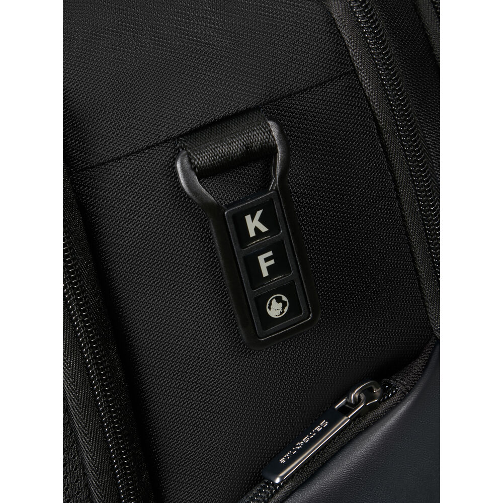 Primo piano di una borsa nera. Presenta una chiusura nera con le lettere 'K' e 'F'. In basso è visibile una cerniera argentata.