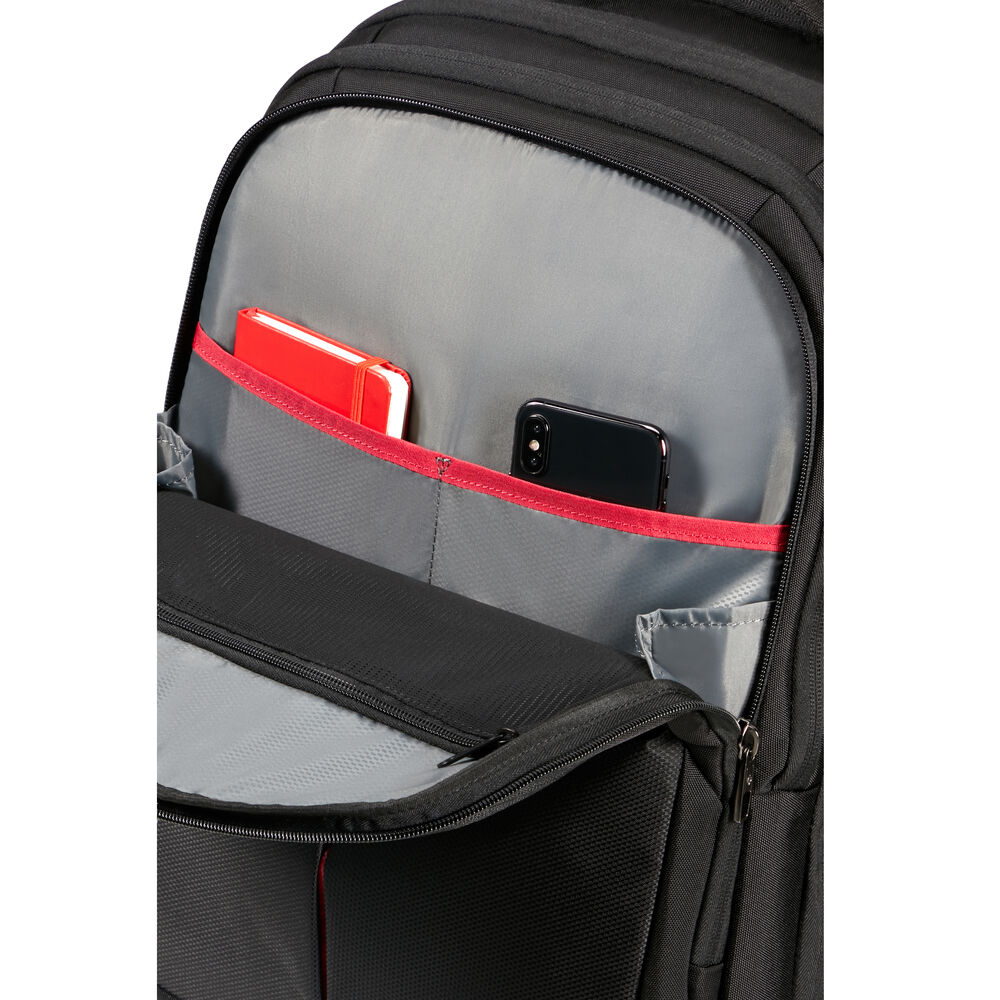 Sac à dos noir ouvert, montrant l'intérieur gris avec des poches bordées de rouge. Un cahier rouge et un téléphone noir sont visibles.