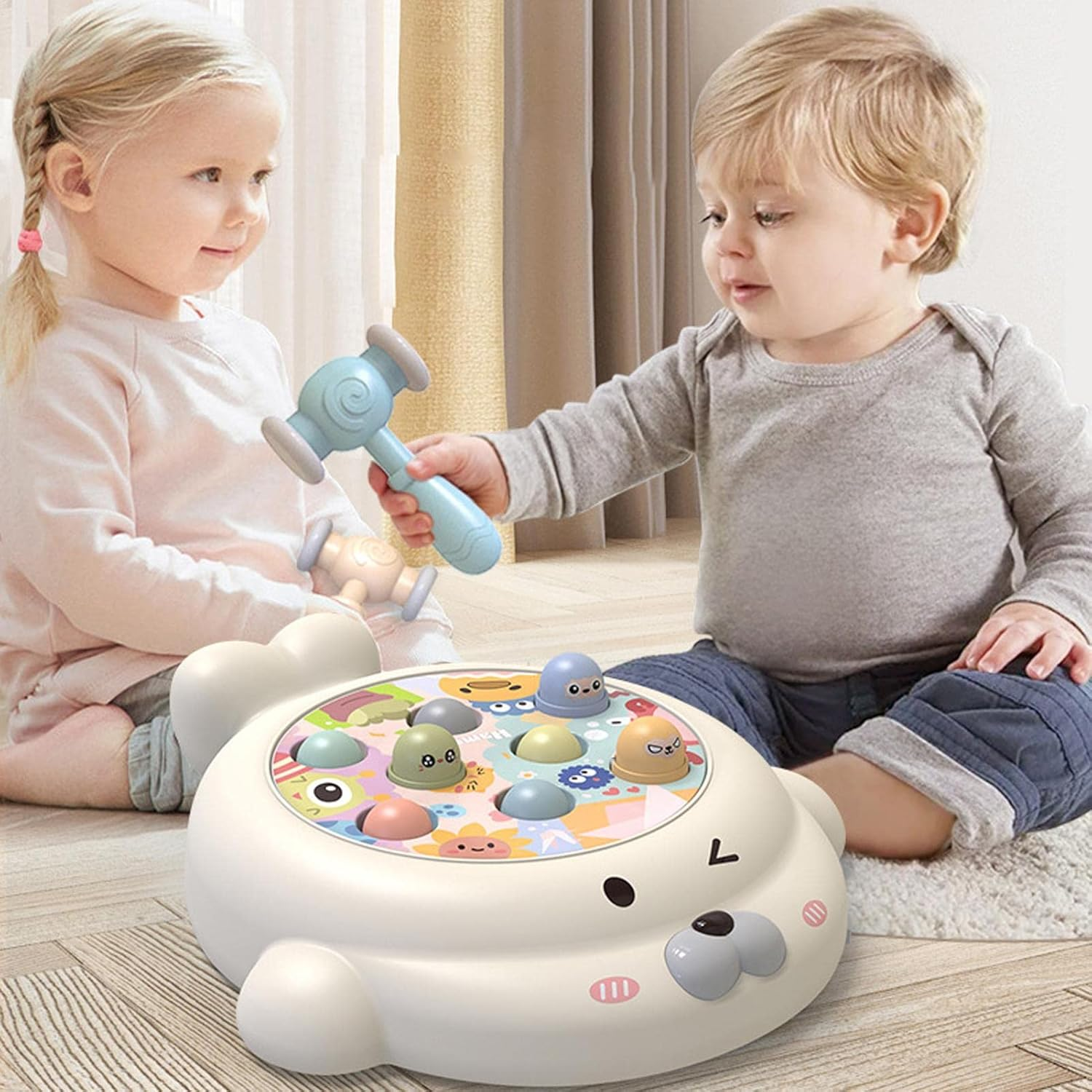 Zwei Kleinkinder spielen mit einem seehundförmigen Spielzeug. Einer hält einen blauen Hammer und schlägt auf bunte Stifte.