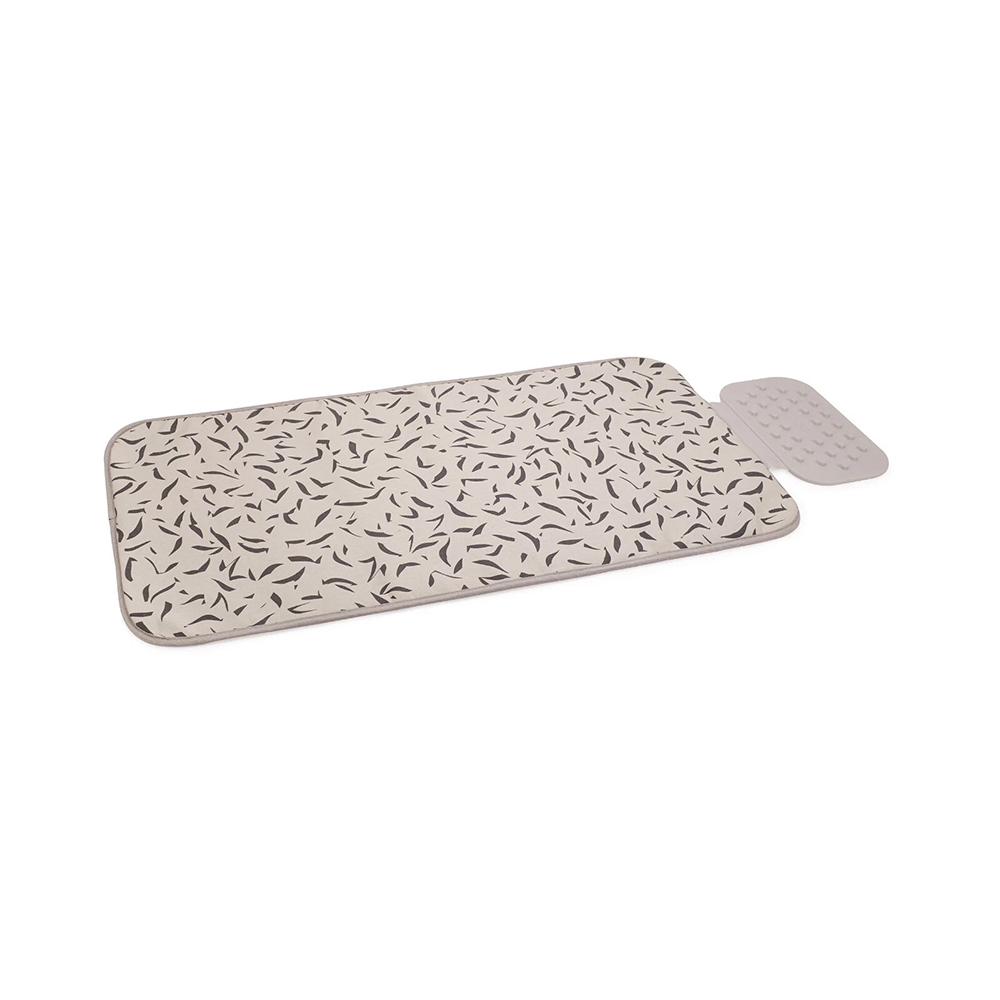 Un cambiador beige con un estampado de hojas y una pequeña almohadilla gris al lado, sobre un fondo blanco.