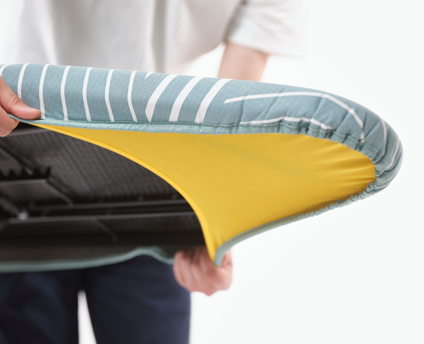 Una persona sostiene una funda de tabla de planchar a rayas verdes y blancas. La funda se tira hacia atrás, revelando una tela amarilla debajo.
