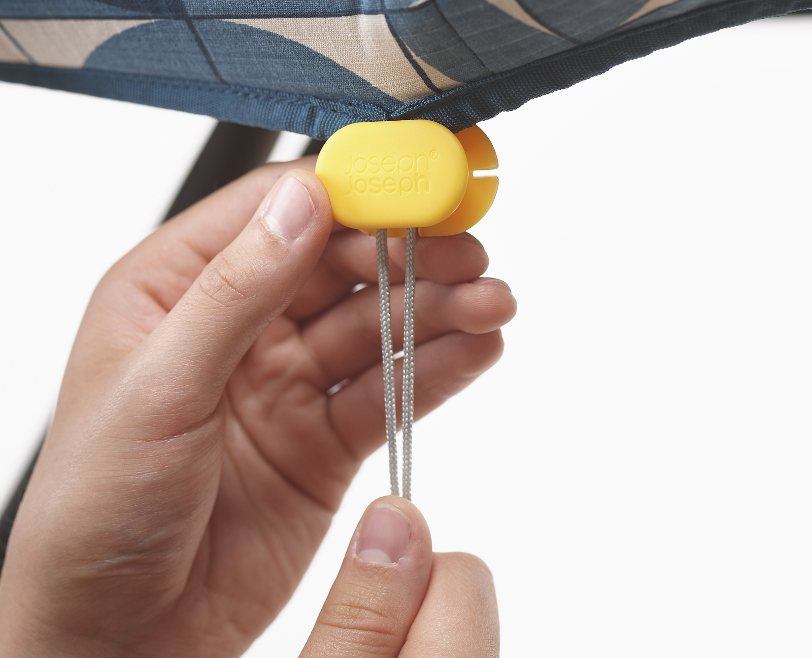 Manos sosteniendo un cierre amarillo con cuerdas grises, sujeto a un paraguas estampado. Fondo blanco.