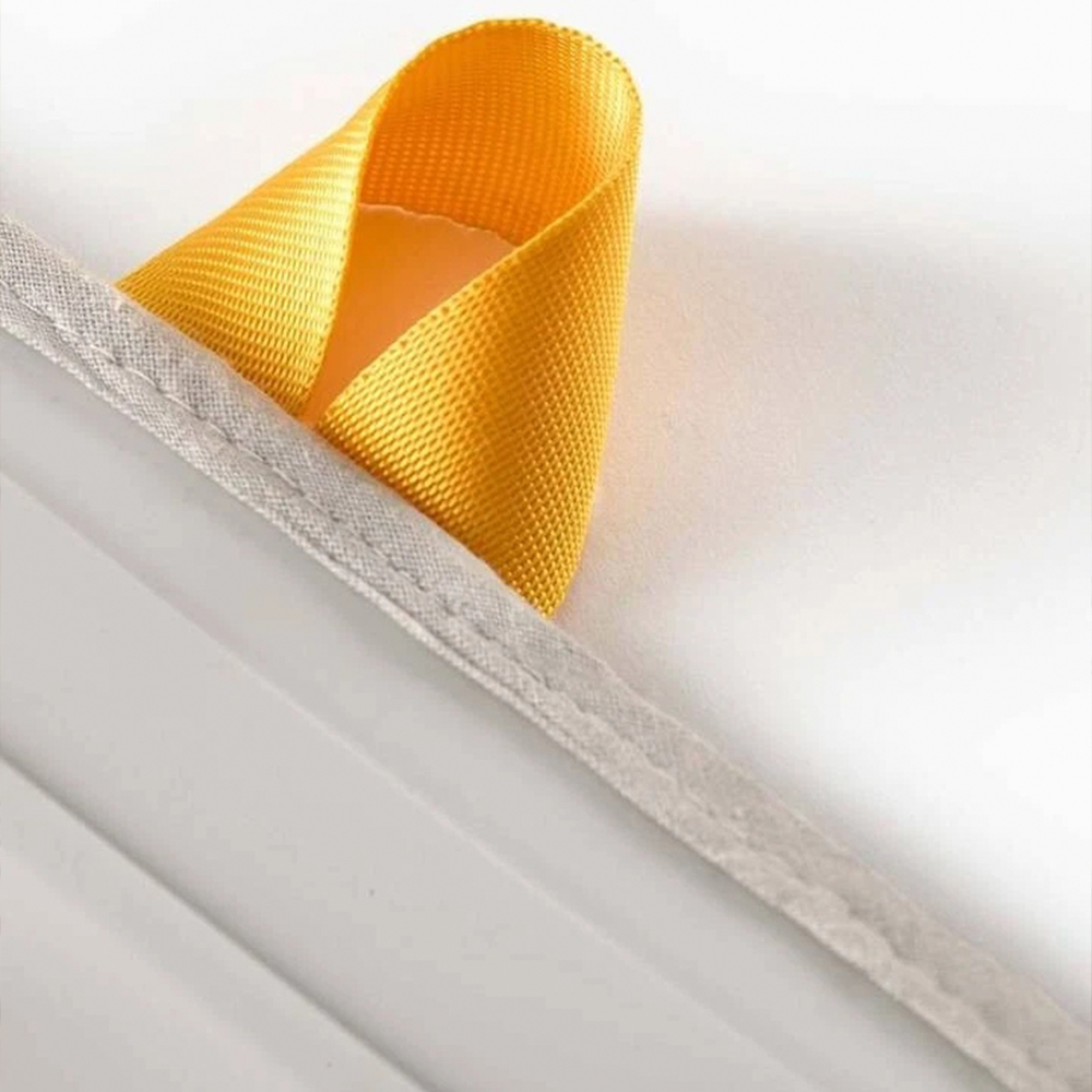 Primer plano de un lazo amarillo sobre una superficie blanca. Un borde gris cosido corre en diagonal.