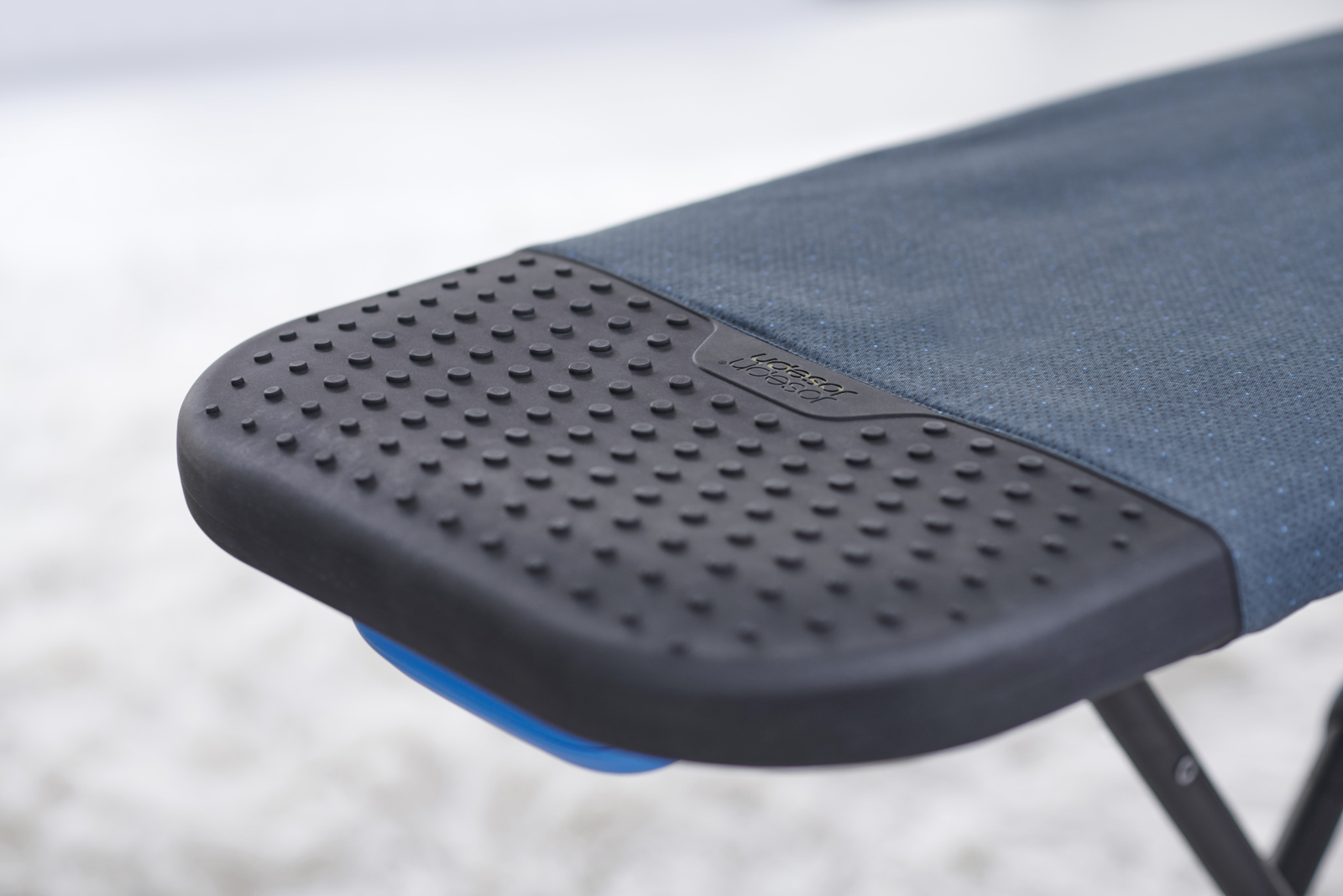 Primer plano de una silla azul y negra. La silla tiene una base de goma negra texturizada y un asiento de tela azul, con la marca visible.