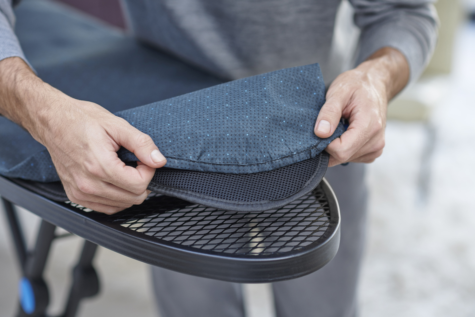 Una persona sostiene un asiento acolchado azul sobre una silla de metal negra. El asiento tiene un patrón de puntos.