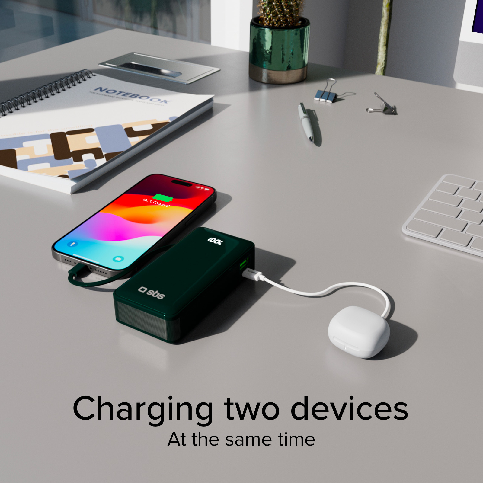 Ein Telefon und Ohrhörer werden von einer grünen Powerbank aufgeladen. Ein Notizbuch, ein Stift und ein Kaktus sind in der Nähe. Das Telefon ist zu 100 % geladen.