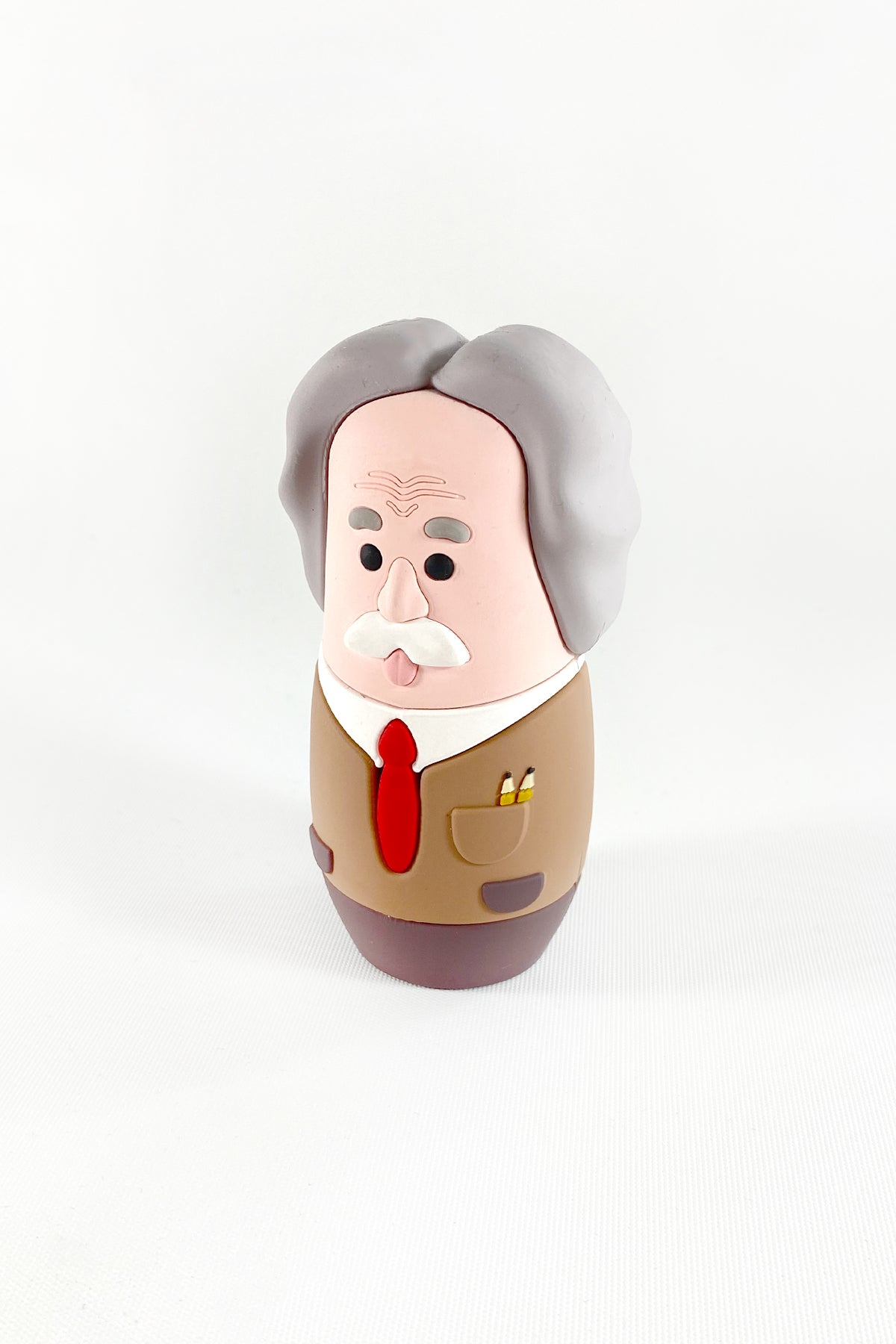 Una statuetta dei cartoni animati di Albert Einstein, con capelli grigi, cravatta rossa e abito marrone. Lo sfondo è bianco.