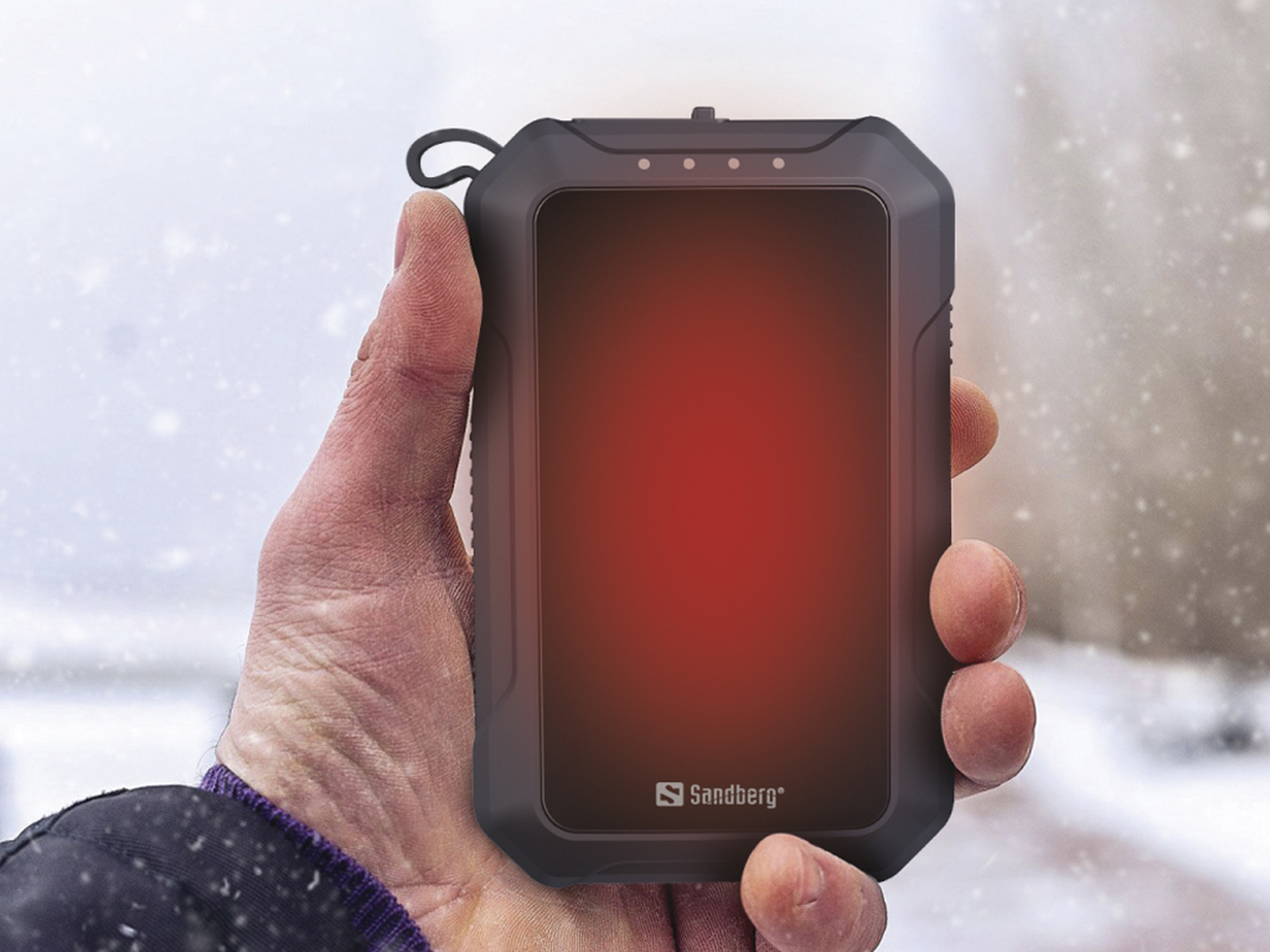 Hand die een donkergrijs Sandberg-apparaat vasthoudt met een rood scherm en drie lampjes bovenop. Besneeuwde achtergrond.