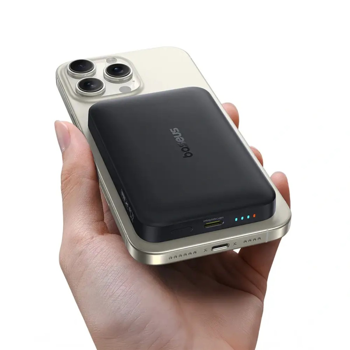 Een hand houdt een telefoon vast met een zwarte powerbank eraan. De telefoon is goudkleurig, de powerbank heeft het merk 'Baseus'.