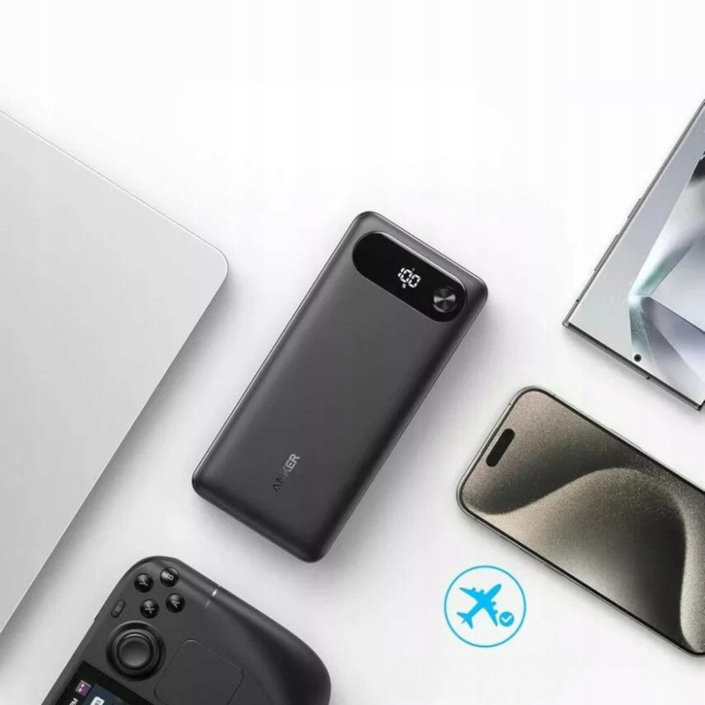 Ciemnoszary power bank Anker z wyświetlaczem naładowania 100%, telefon, tablet i konsola do gier na białej powierzchni.
