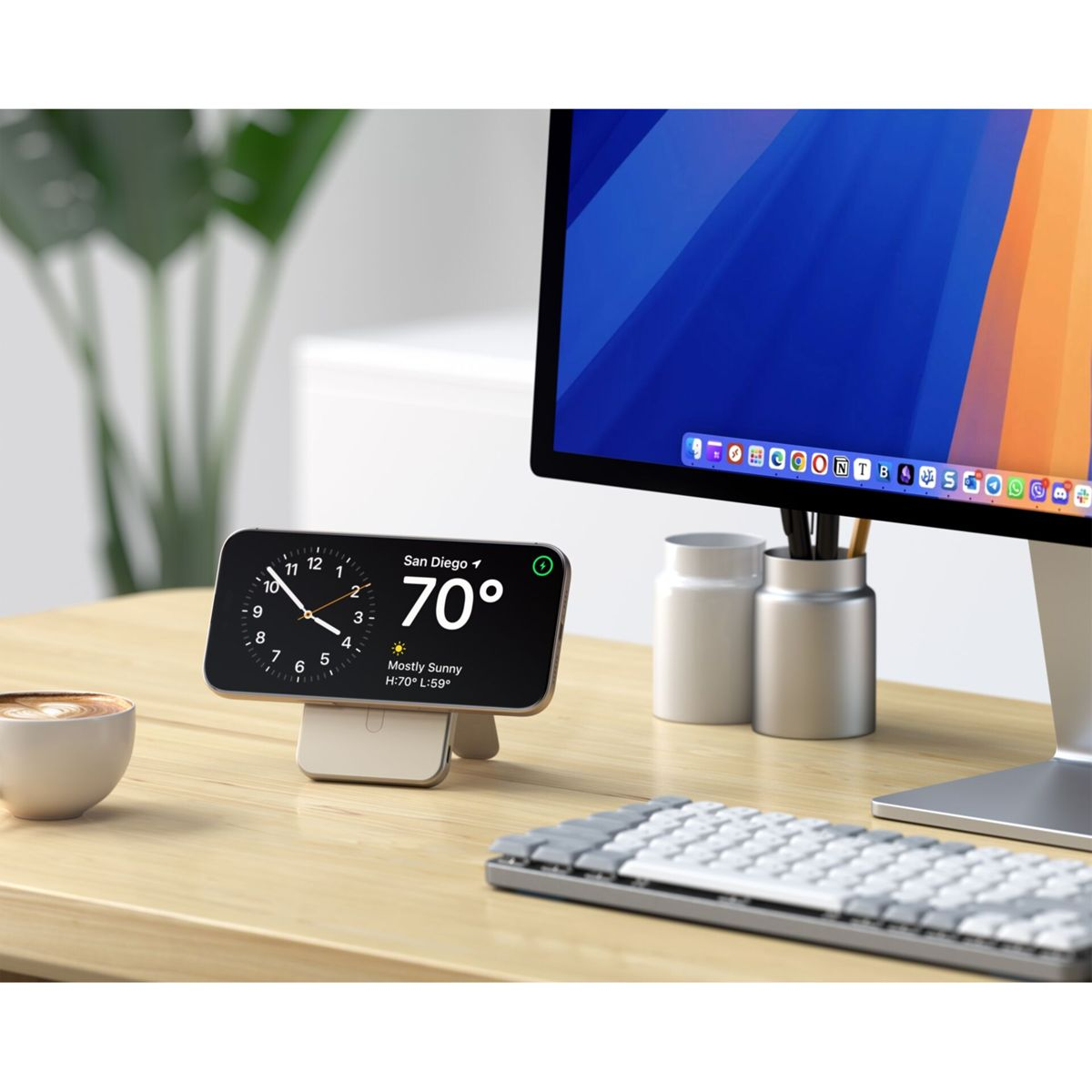 Un telefono che mostra l'ora e il meteo, su una scrivania con tastiera, monitor, tazza di caffè e accessori.
